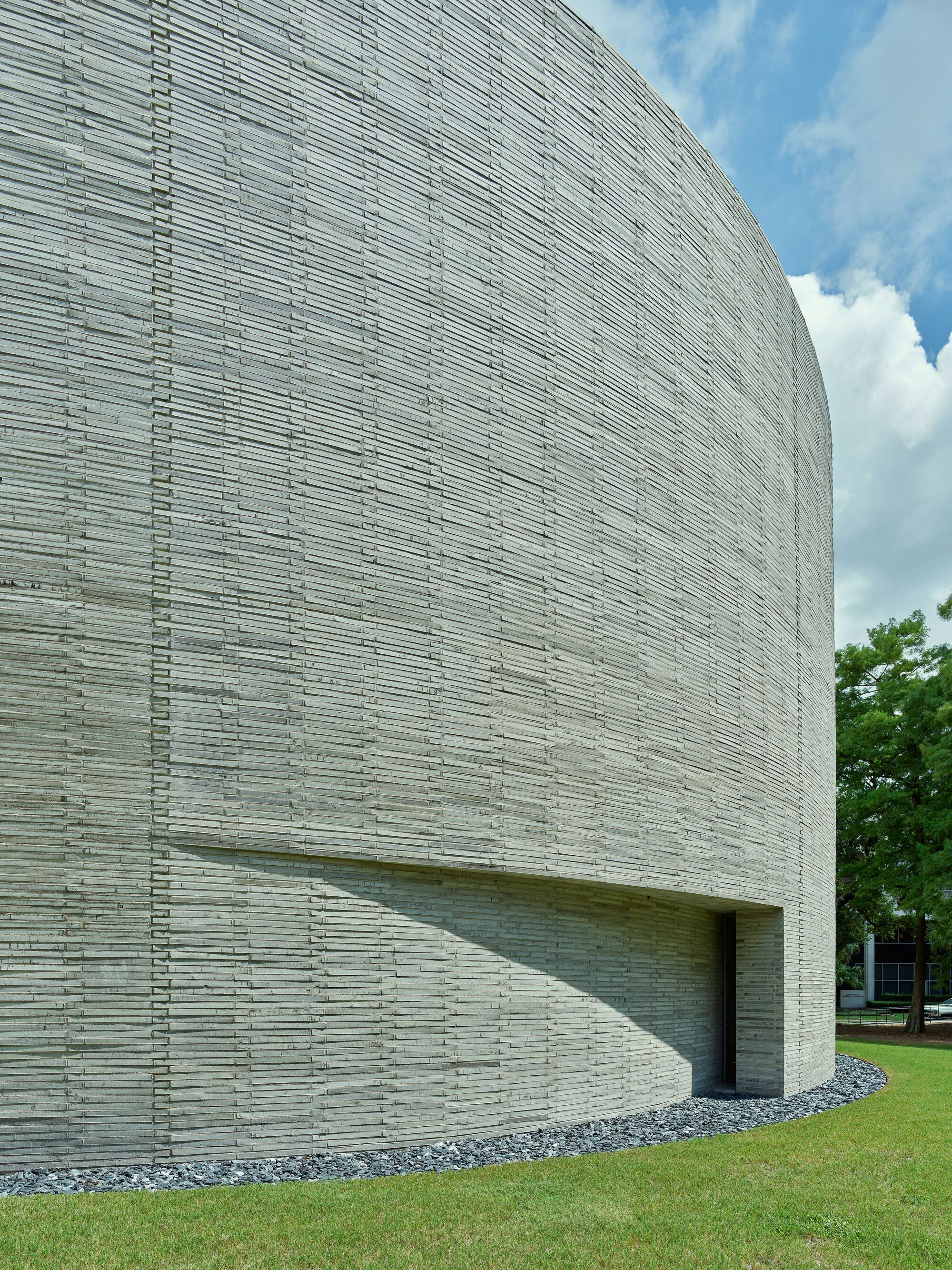 Close-up of the curved brick wall showing recessed entry slot beneath white clouds