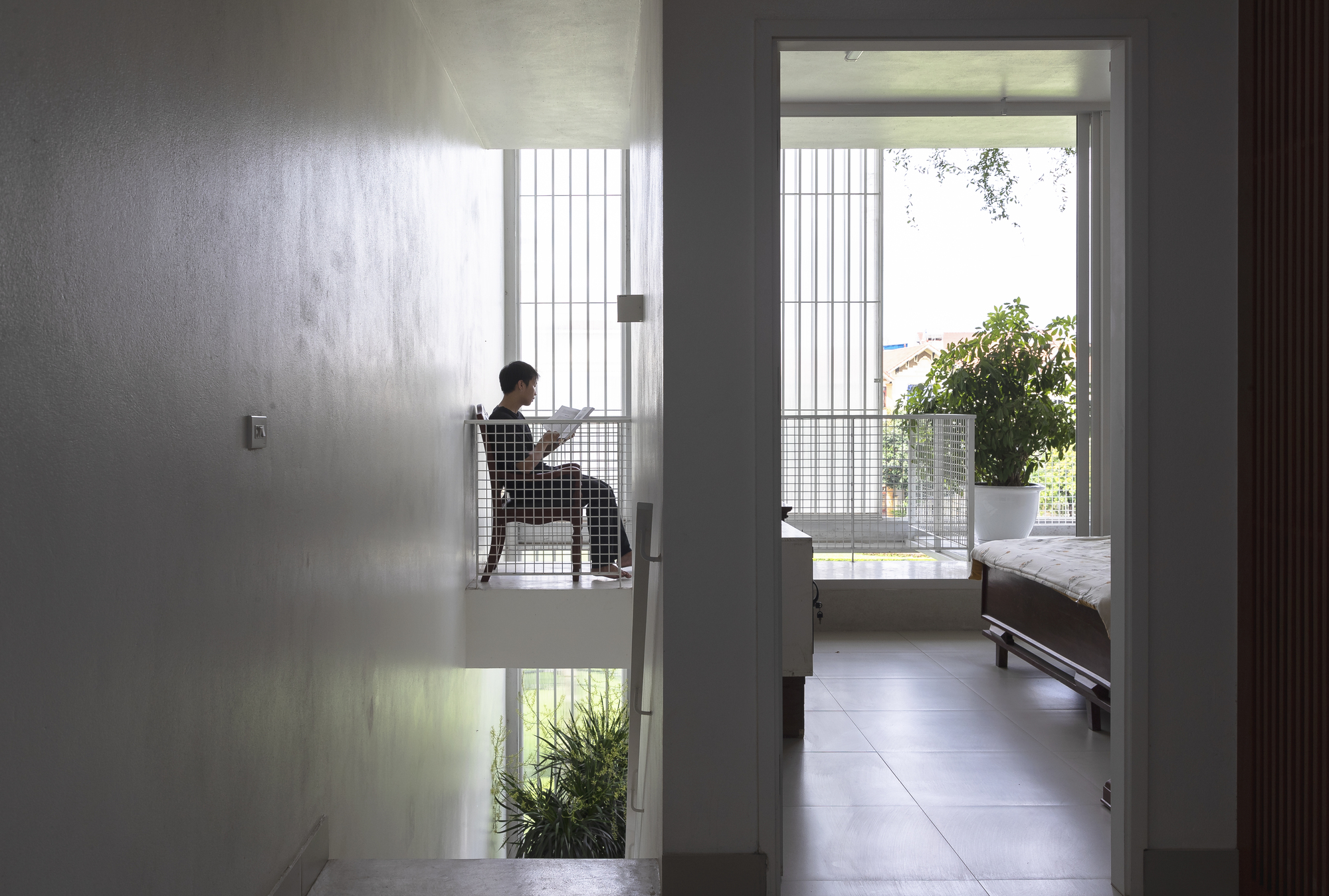 Interior hallway view through doorways to a bedroom with a person seated beside a translucent screen