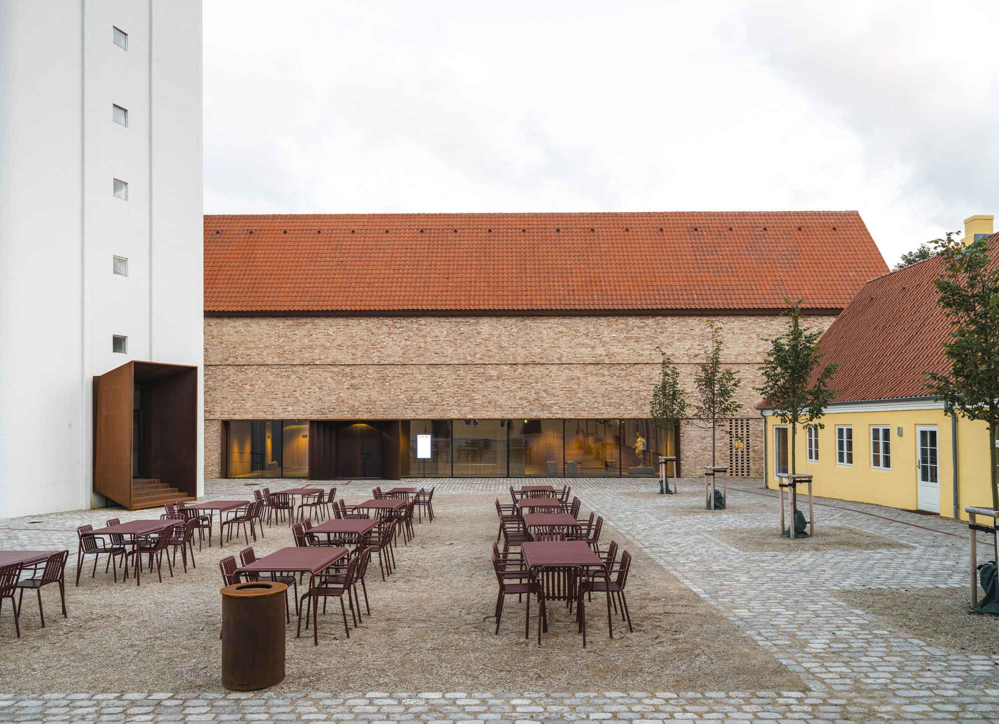 Cobblestone courtyard with burgundy tables and chairs facing a brick building with red tile roof