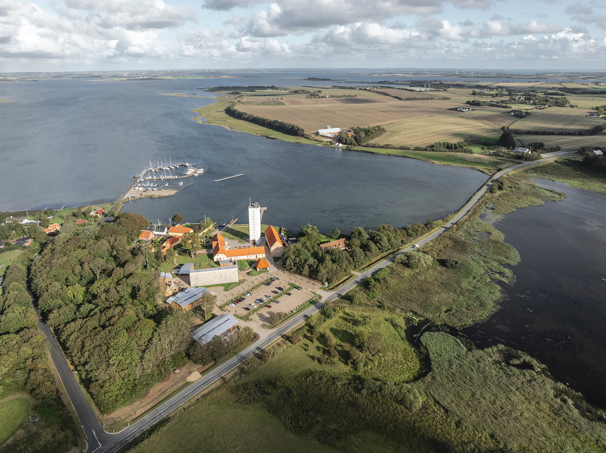 Aerial view of a peninsula with red-roofed buildings and white tower nestled among trees at the water's edge
