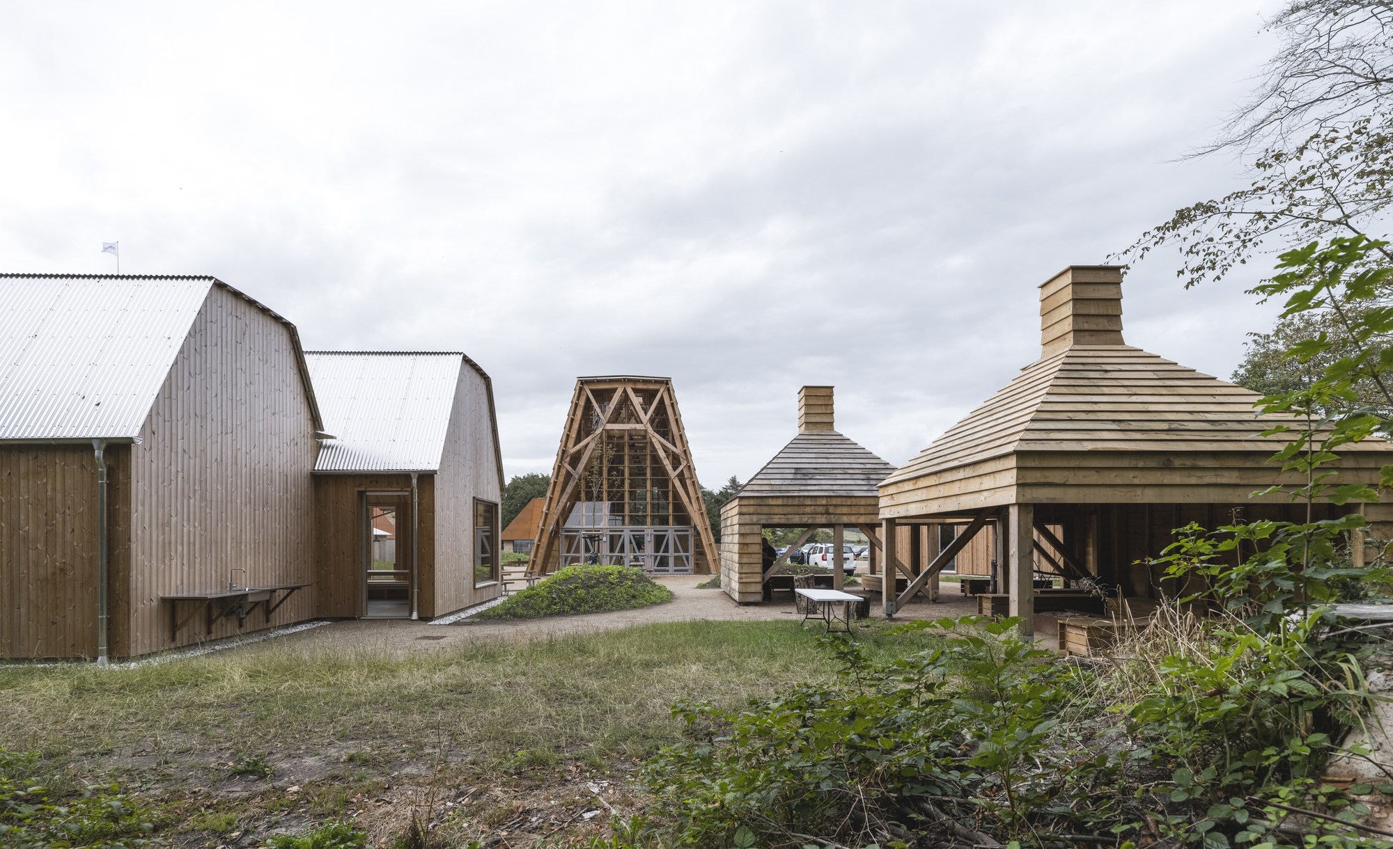 Cluster of timber pavilions with curved and gabled roofs on a grassy hillside under overcast sky