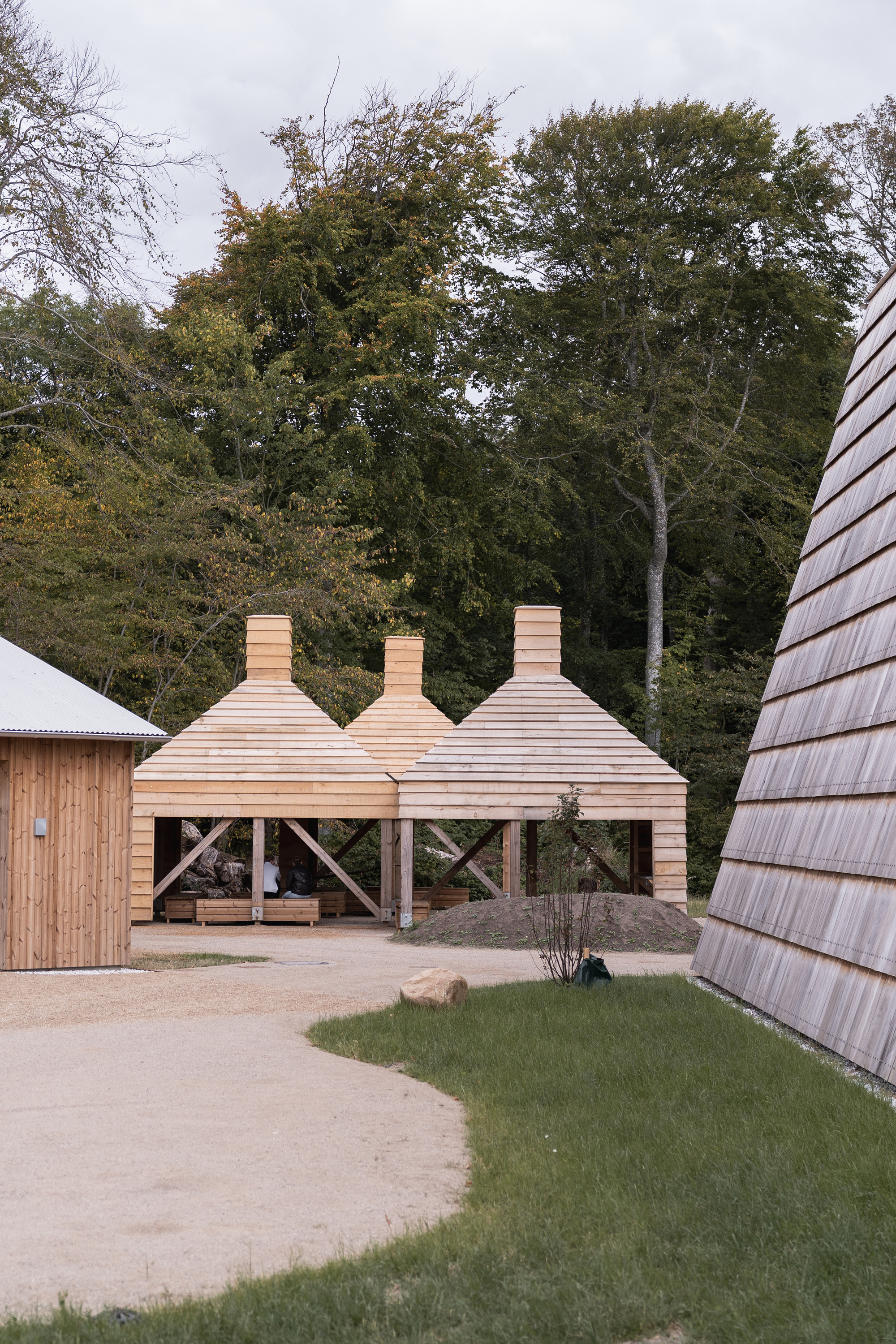 Three horizontal timber pavilions with stacked chimney forms amid lawn and mature trees