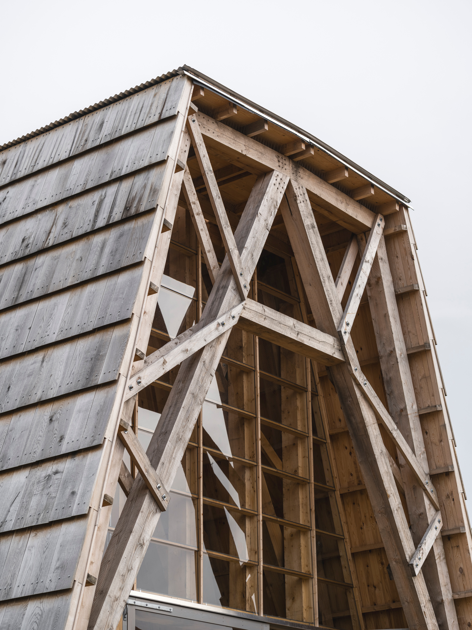 Exposed timber diagonal bracing within a gabled facade opening clad in weathered horizontal siding