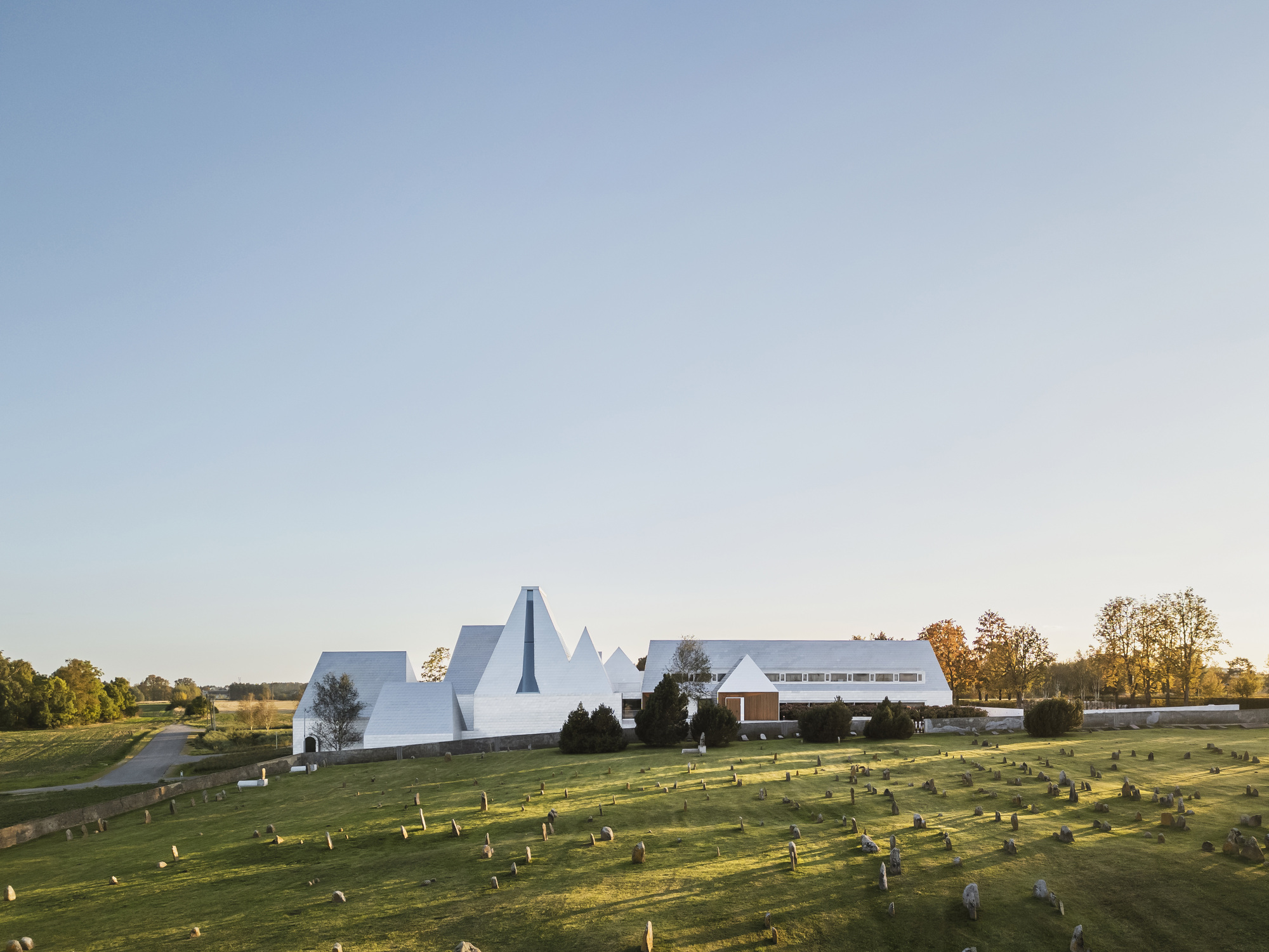 Clustered peaked white roofs and horizontal wing overlooking a grassy burial ground in afternoon light