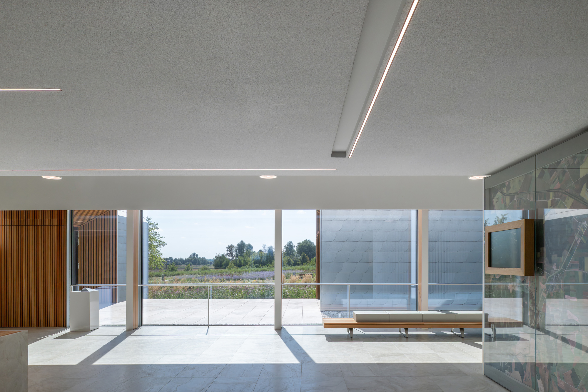 Interior hall with flush ceiling light slots and floor-to-ceiling glazing overlooking an open courtyard