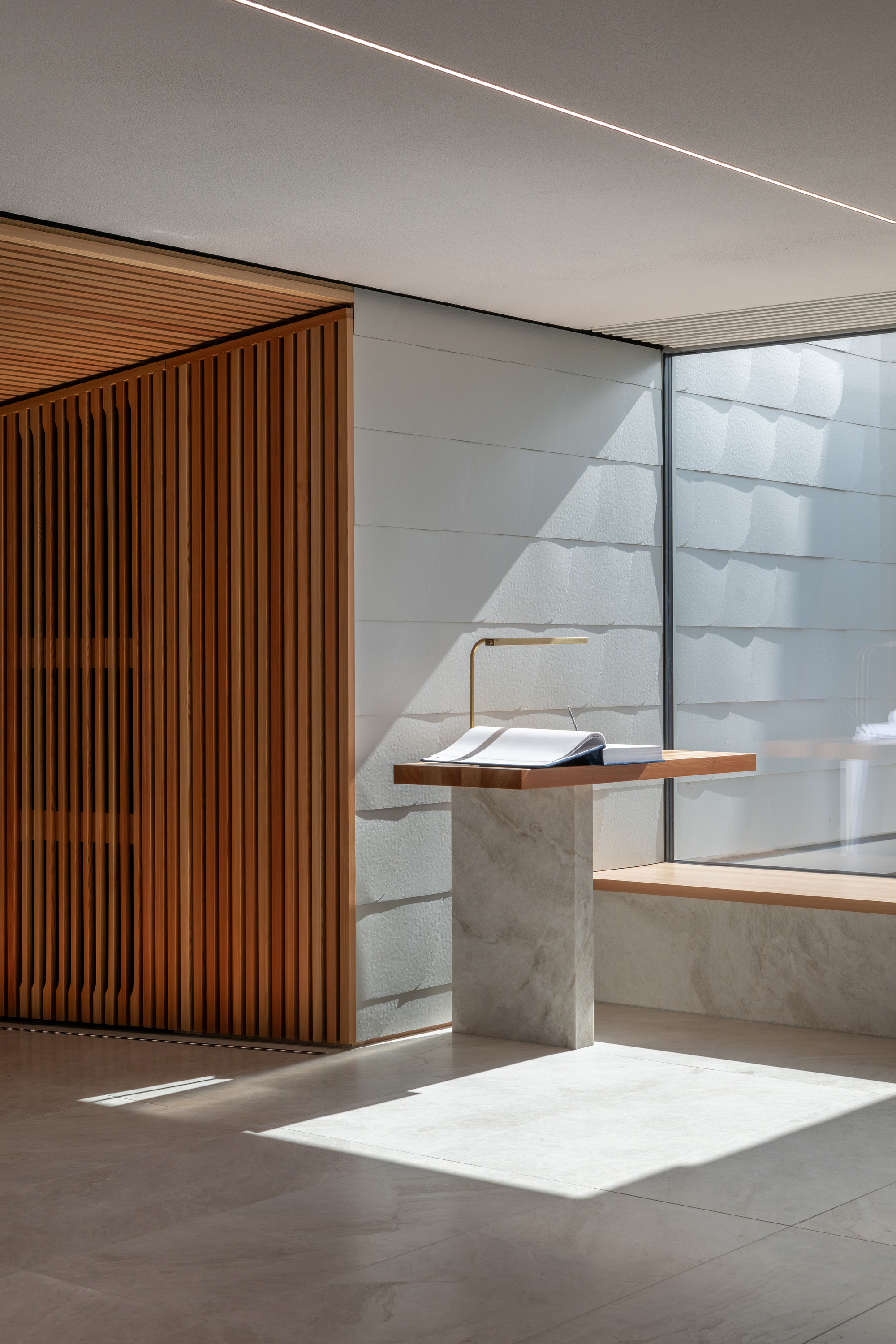 Interior lectern of concrete and timber beside vertical wood slat wall with sunlight filtering through