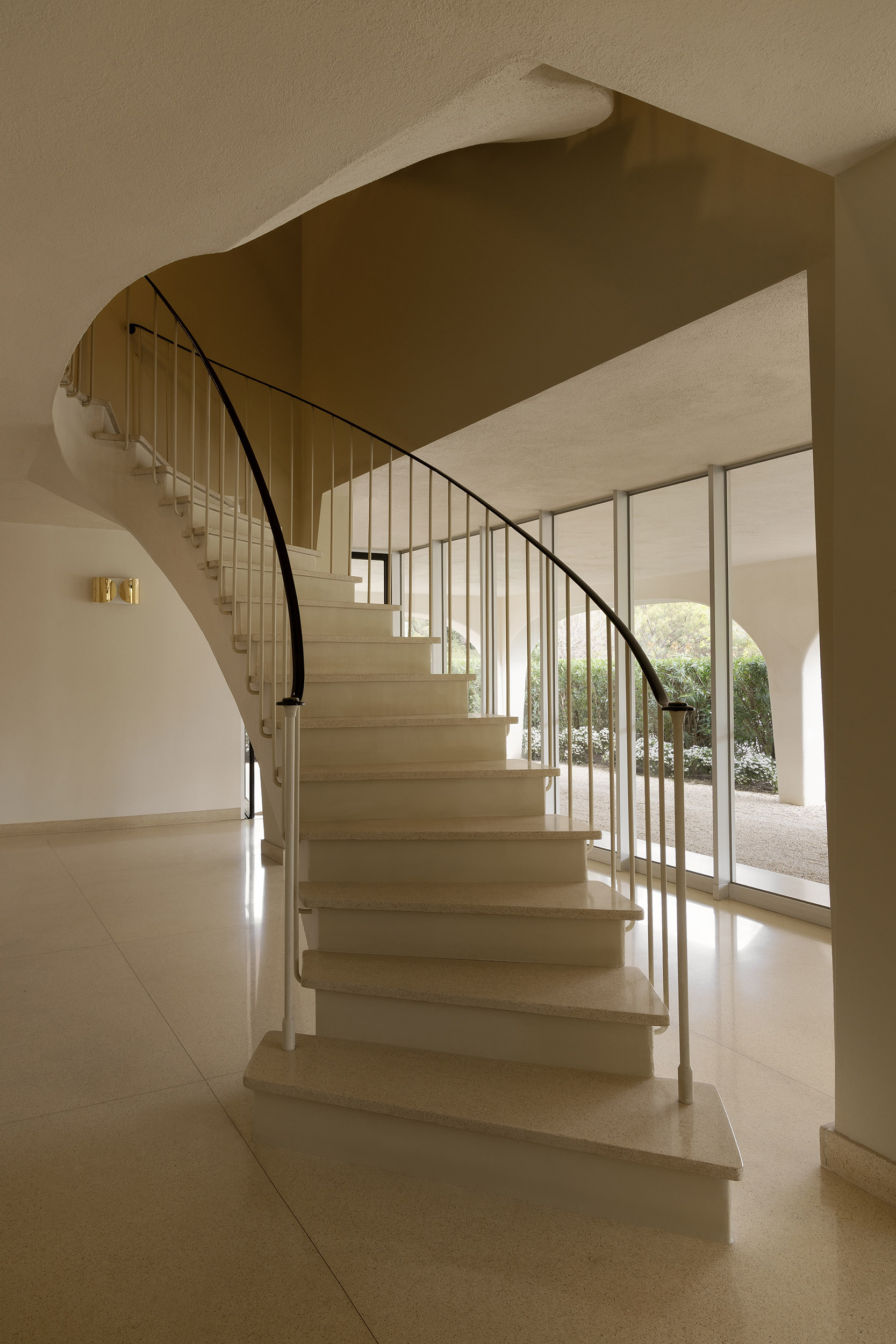 Curved stone staircase with steel rod balustrade and glass doors opening to a courtyard