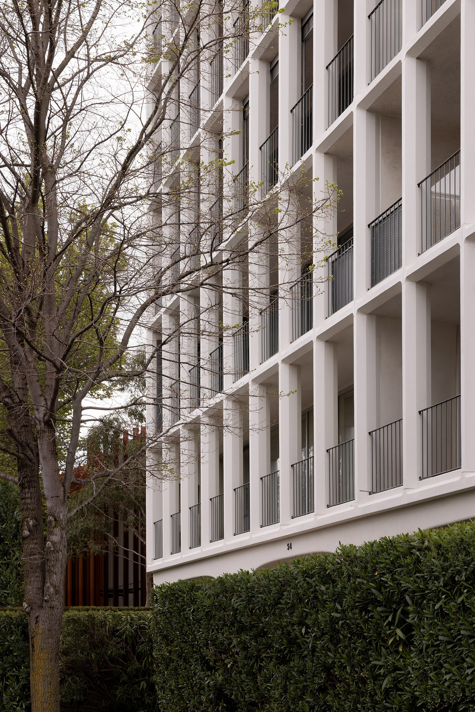 Oblique view of the facade showing concrete columns and balconies with bare tree branches