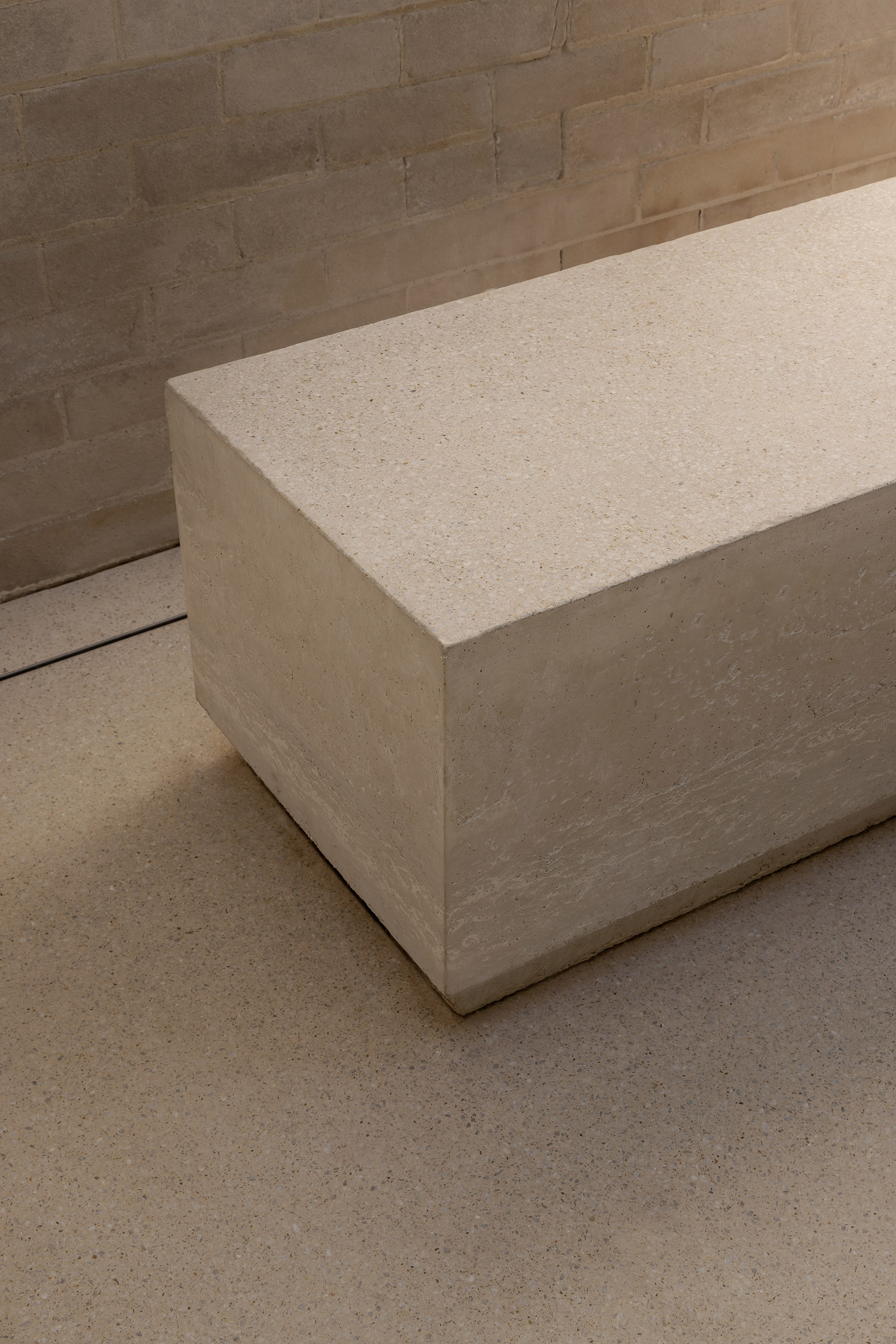 Corner detail of cast stone bench against brick wall with terrazzo floor