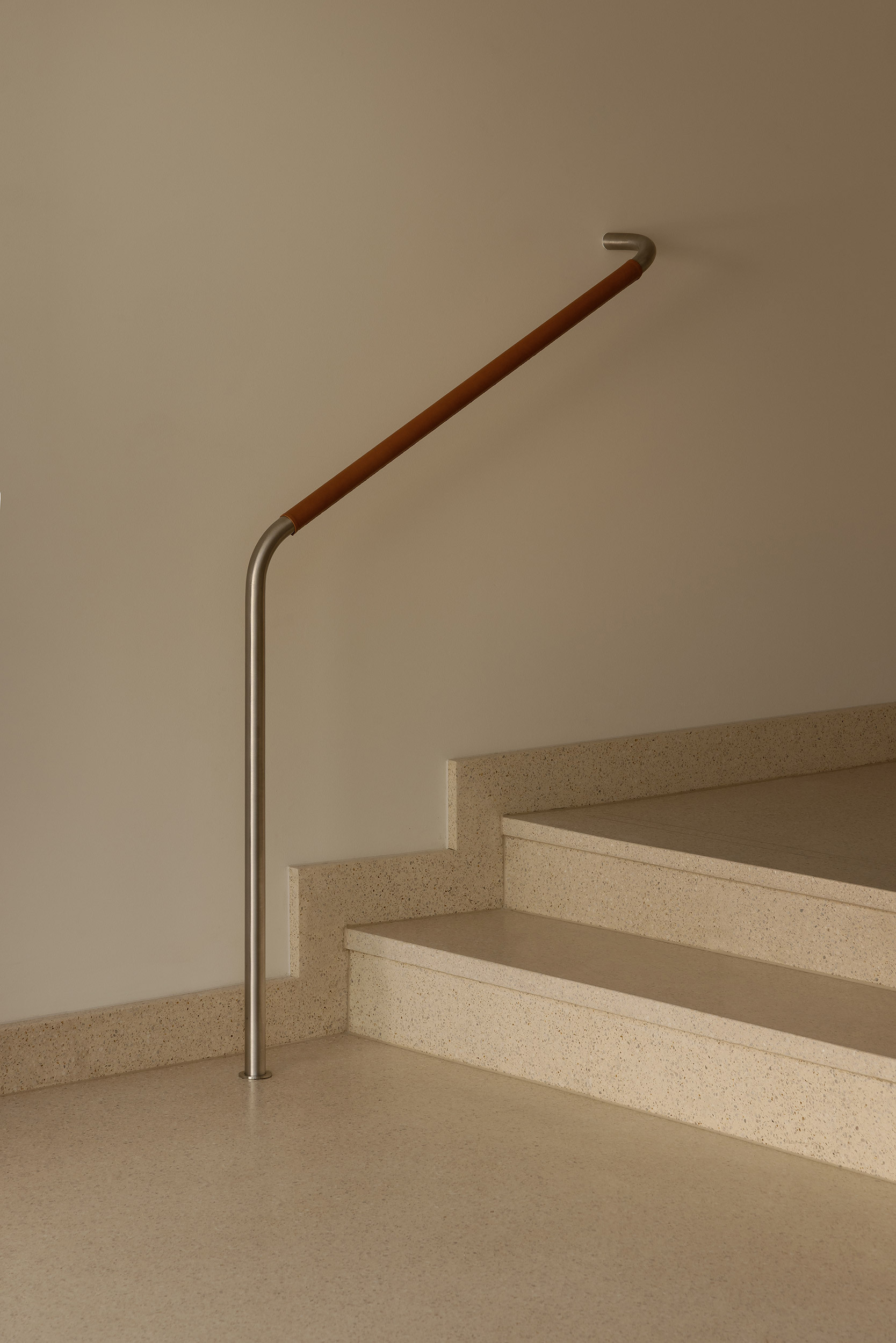 Staircase with terrazzo treads and leather-wrapped handrail terminating at brushed metal base