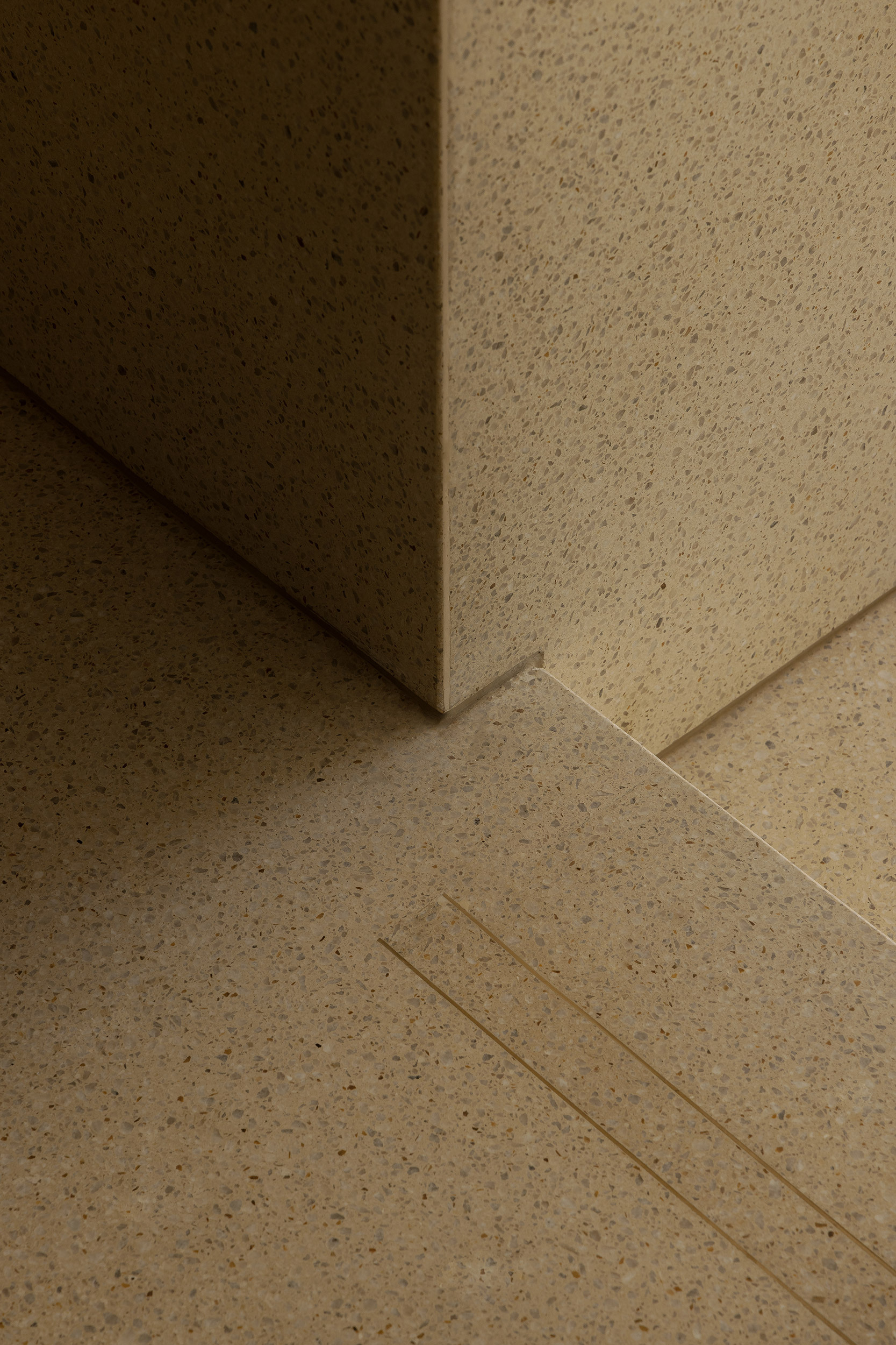 Close-up of terrazzo flooring meeting a wall corner with integrated drainage channel under warm light