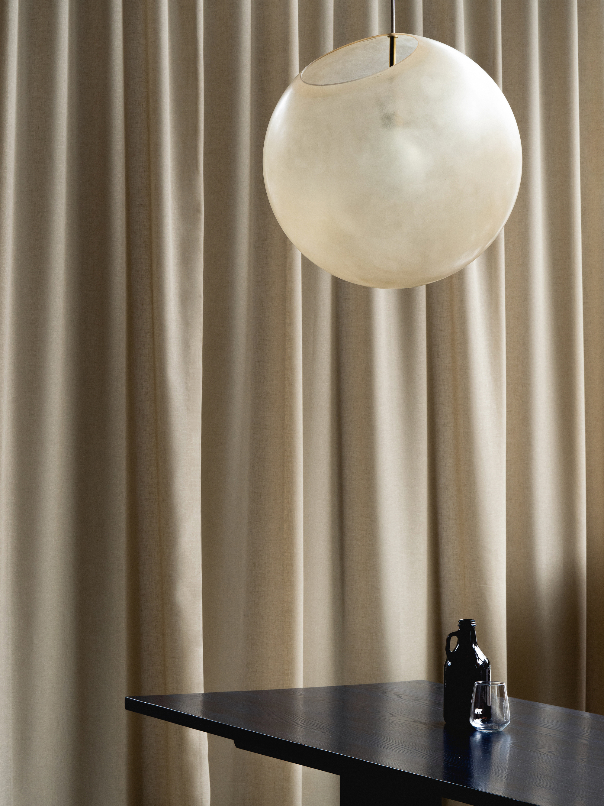 Spherical pendant light suspended above a dark table with bottle and glass against pleated fabric backdrop