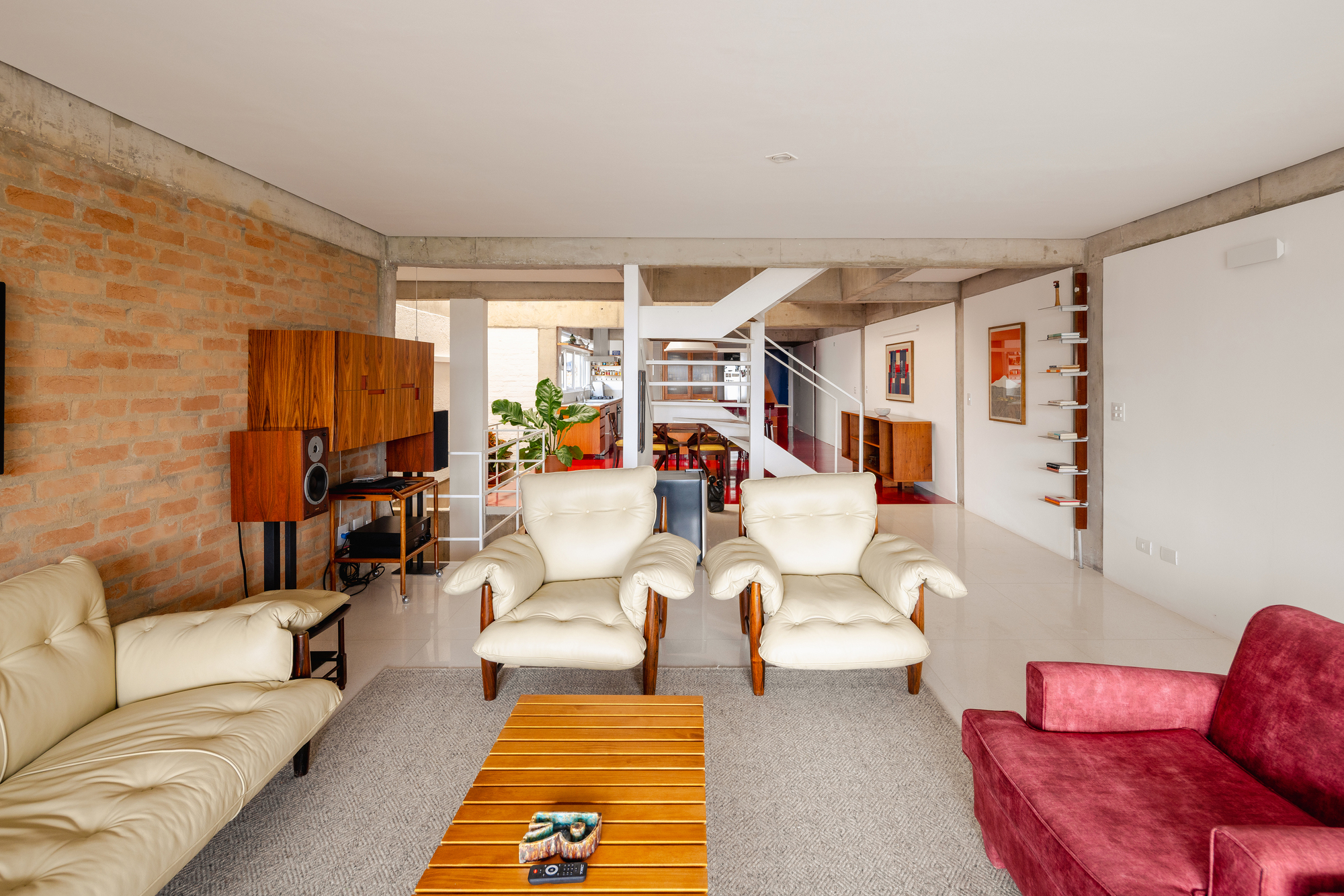 Living area with exposed concrete beams and view through to dining room and white staircase beyond