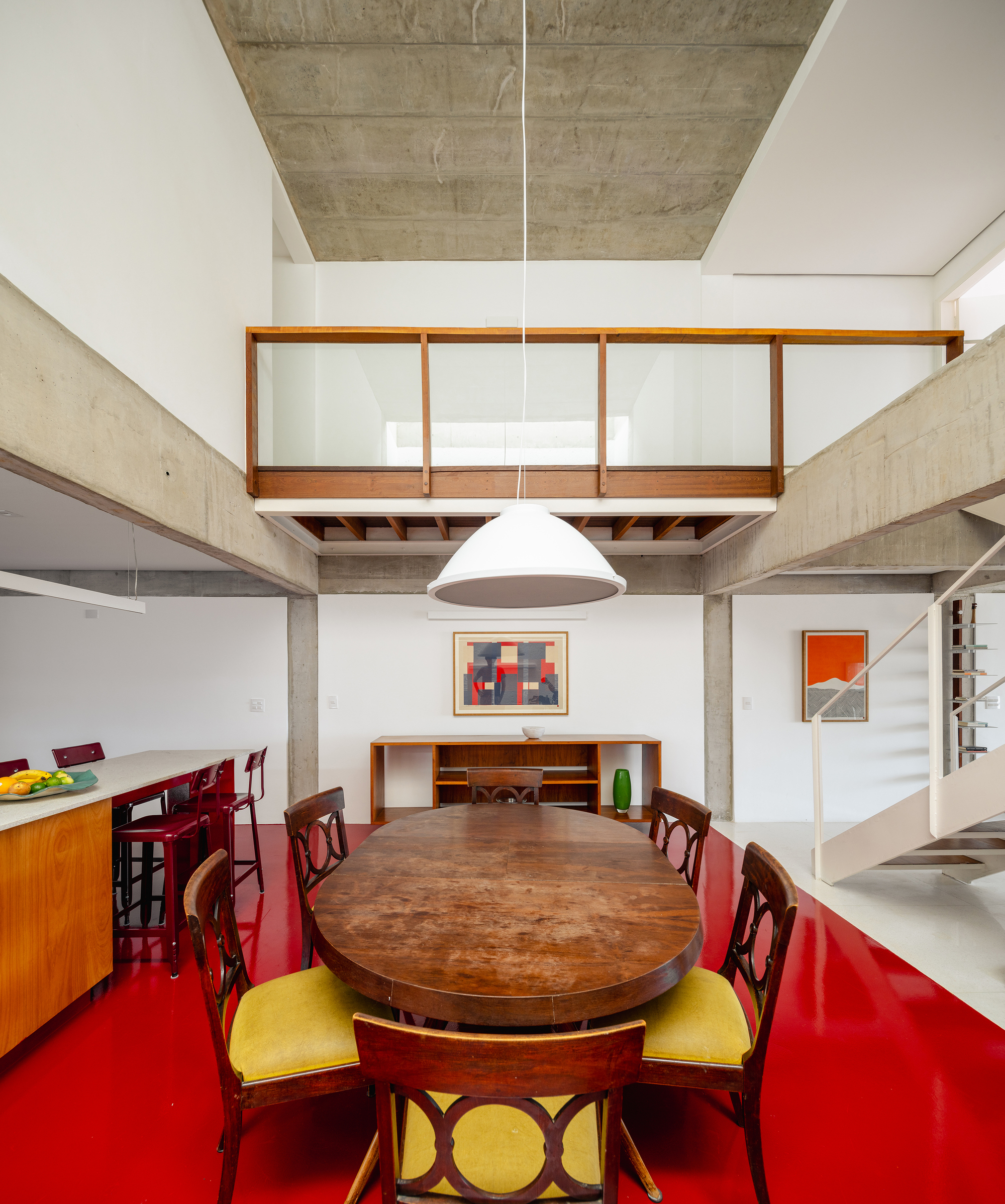Double-height dining room with red epoxy floor, timber-framed mezzanine balcony and suspended pendant light