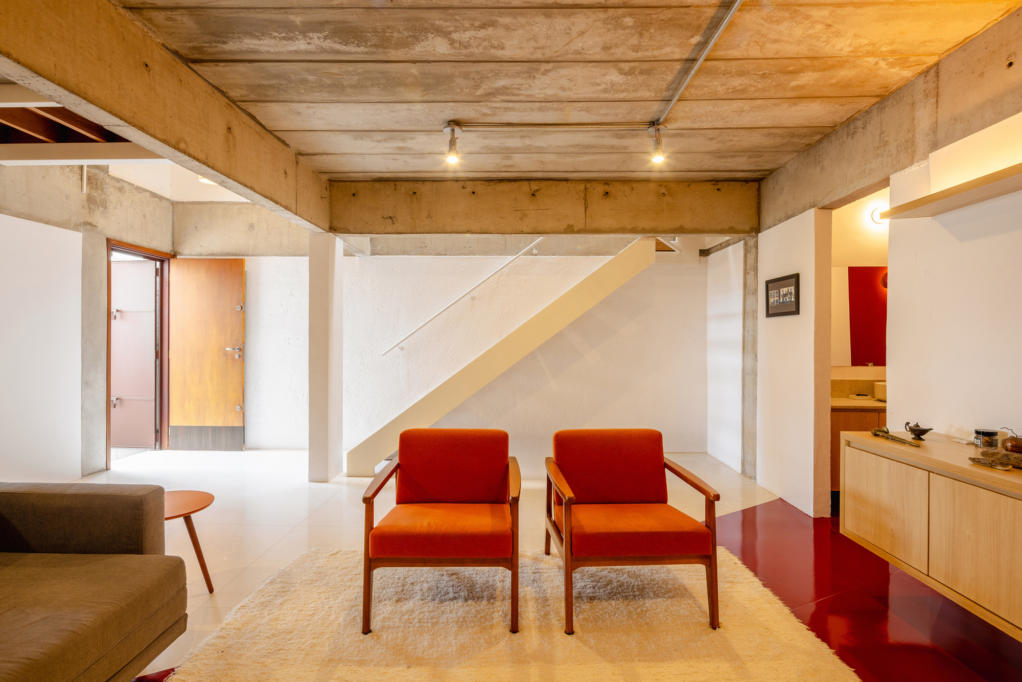 Double-height living room with exposed concrete ceiling beams and plywood walls above white volumes