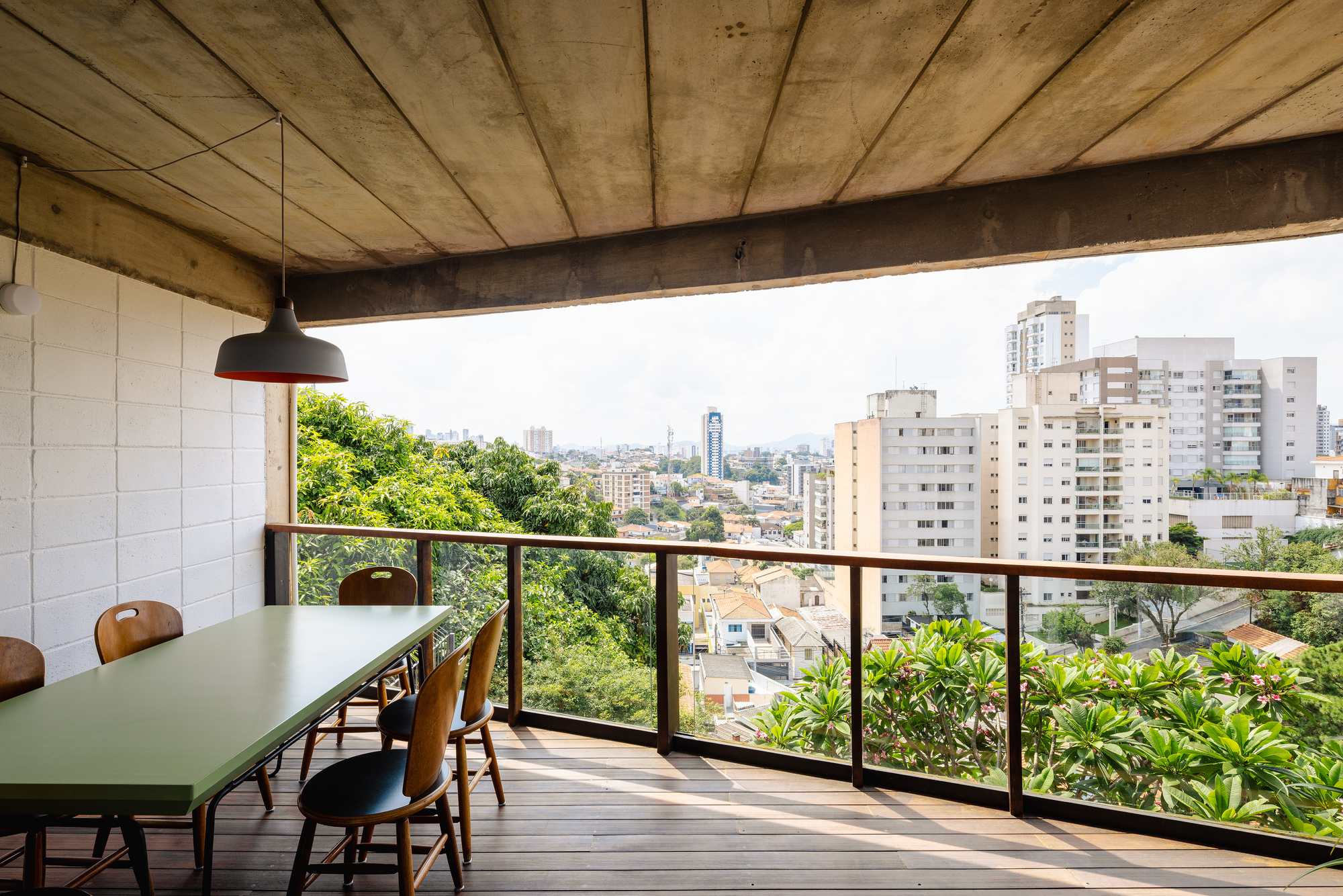 Dining terrace with timber decking and metal railing overlooking a green neighborhood and distant towers