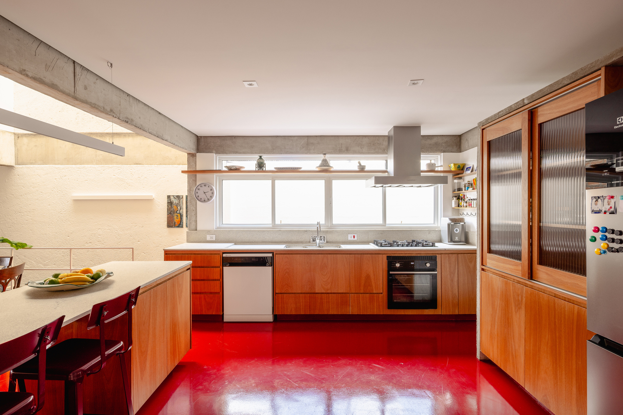 Kitchen galley with wood cabinetry and stainless appliances on a bright red resin floor