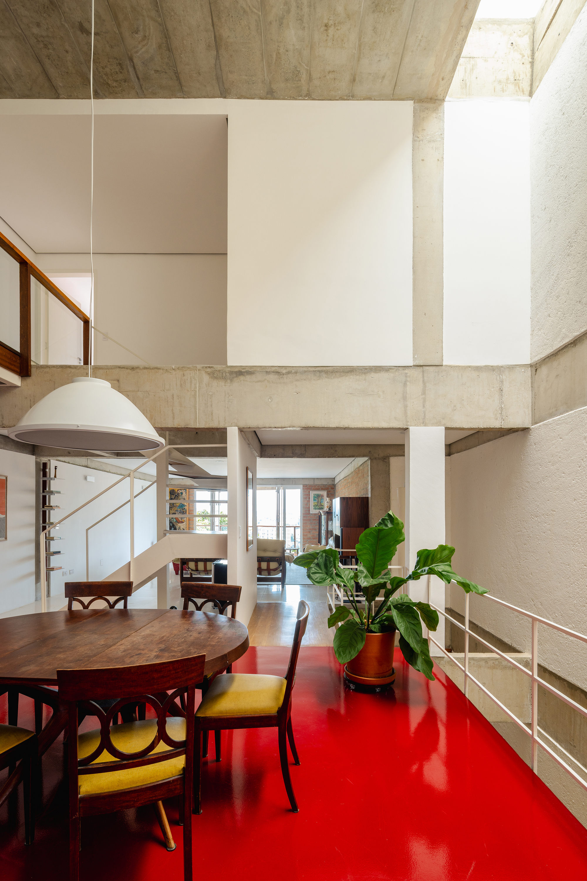 Double-height dining area with red resin floor, exposed concrete beams, and potted banana plant