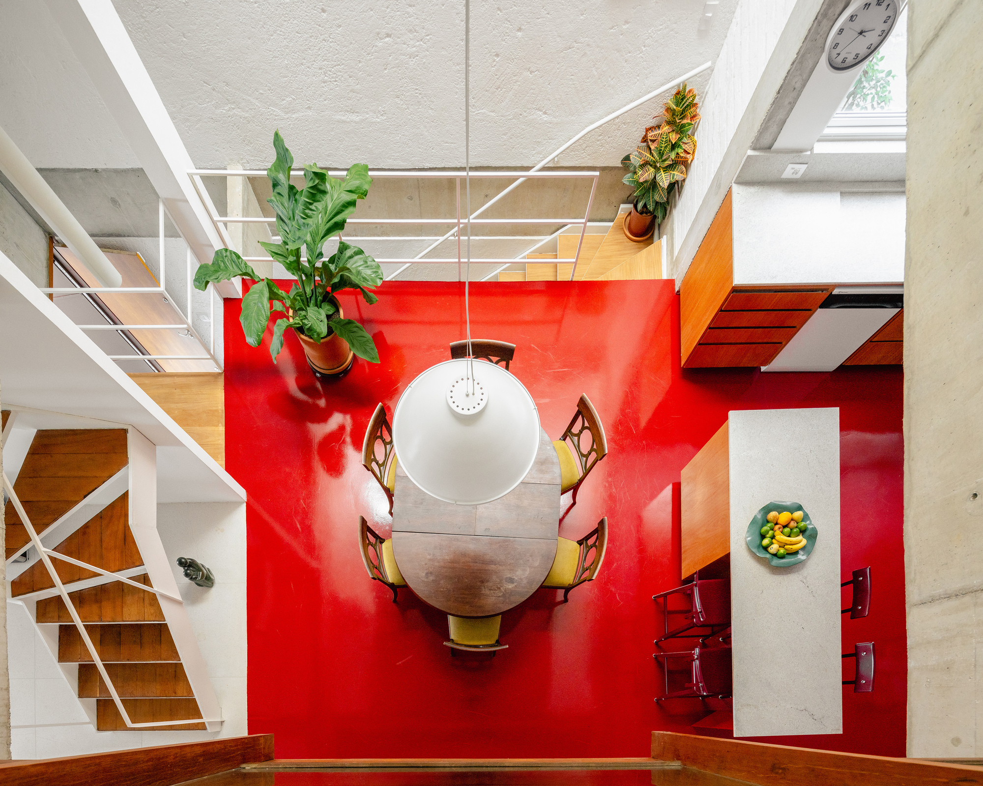 Overhead view of round dining table on red floor with white metal railings and wood cabinetry