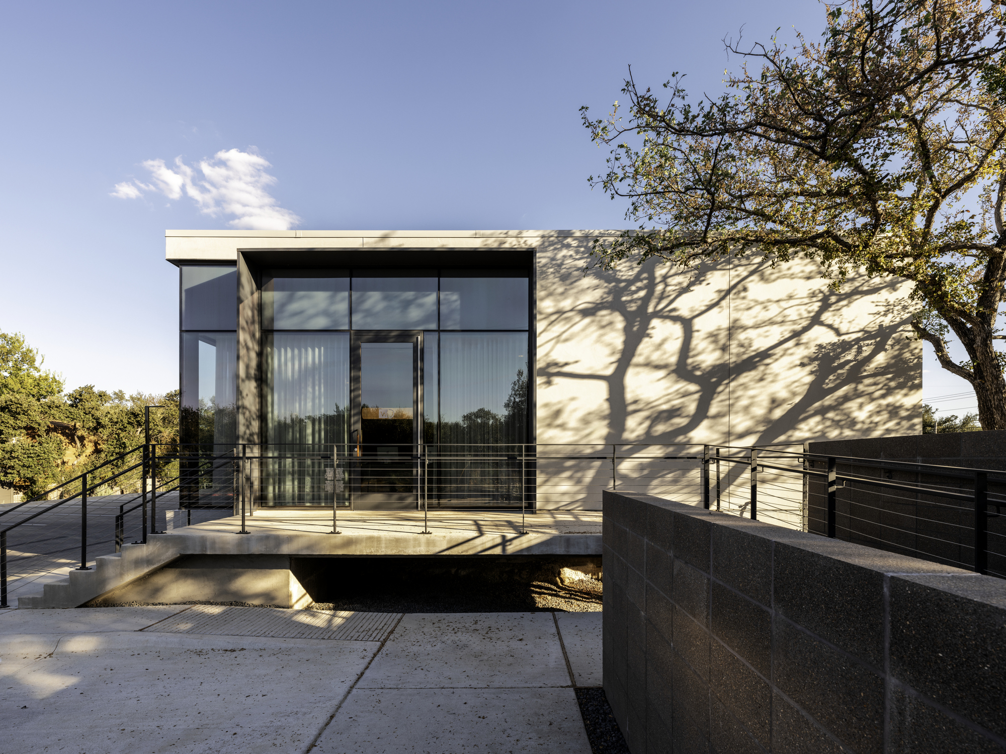Rear elevation showing the glass corner with tree shadows falling across the white panel facade