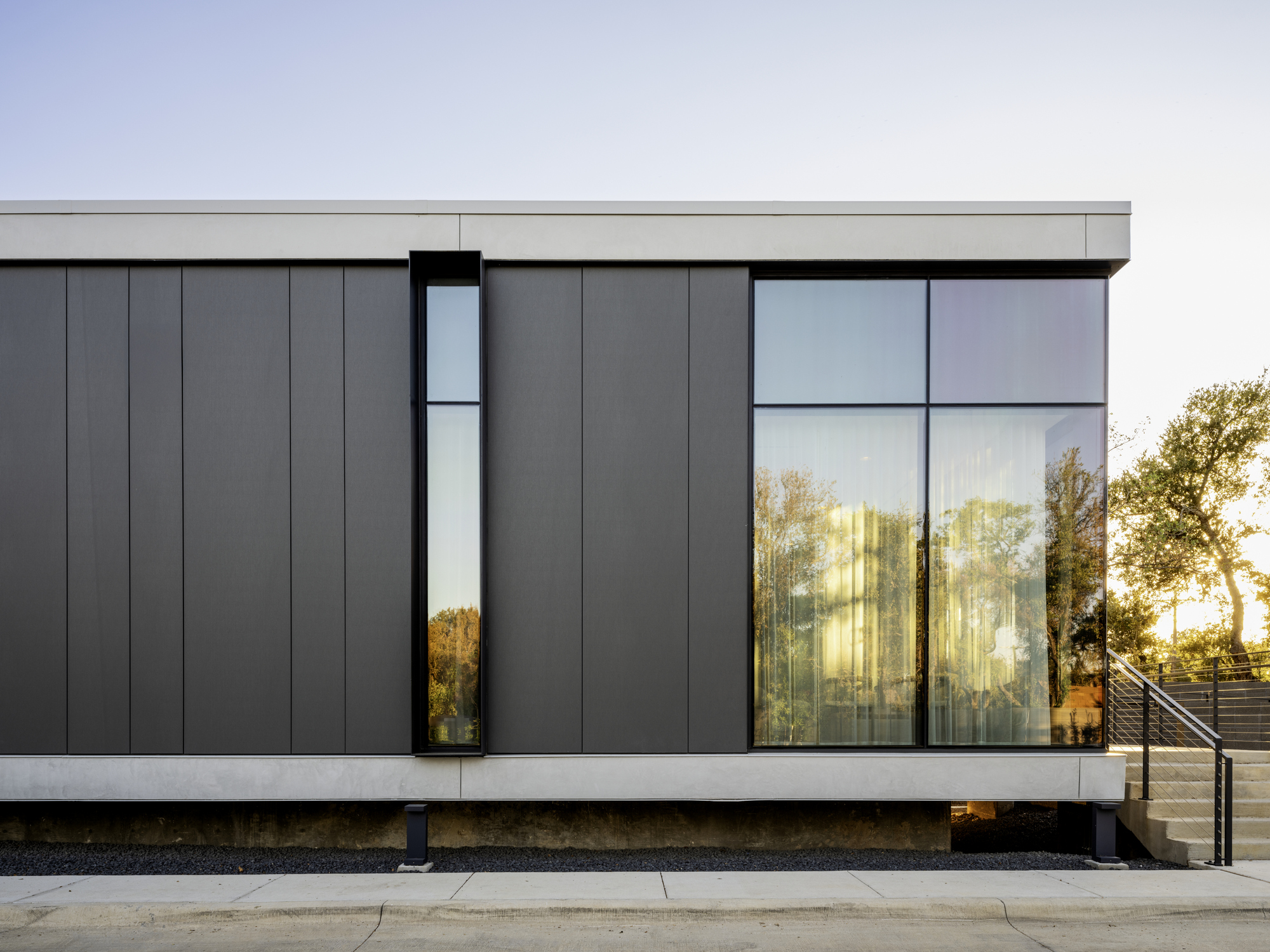 Dark metal panel facade with narrow vertical window and large glass opening at dusk