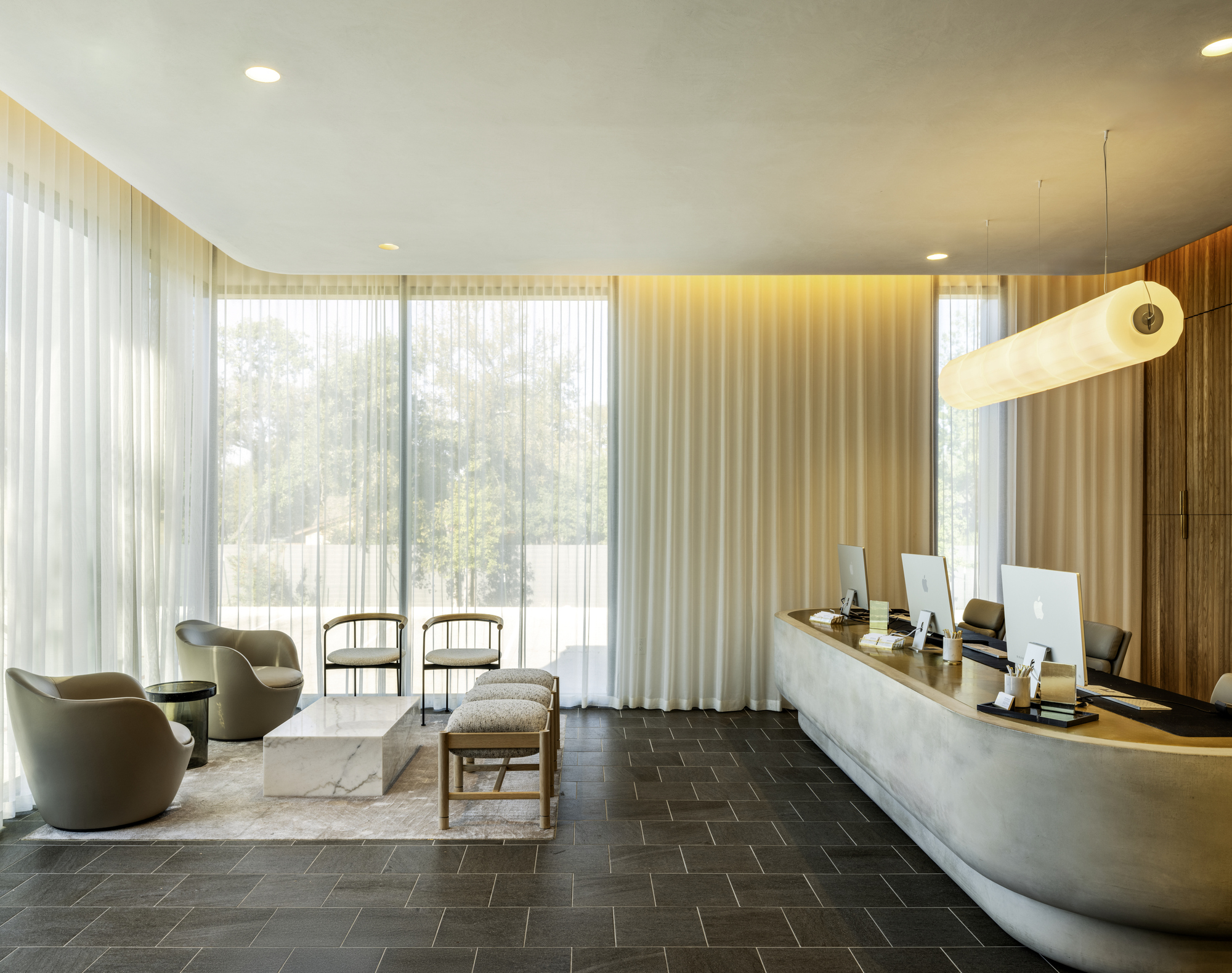 Reception area with curved desk, dark herringbone floor and floor-to-ceiling sheer curtains