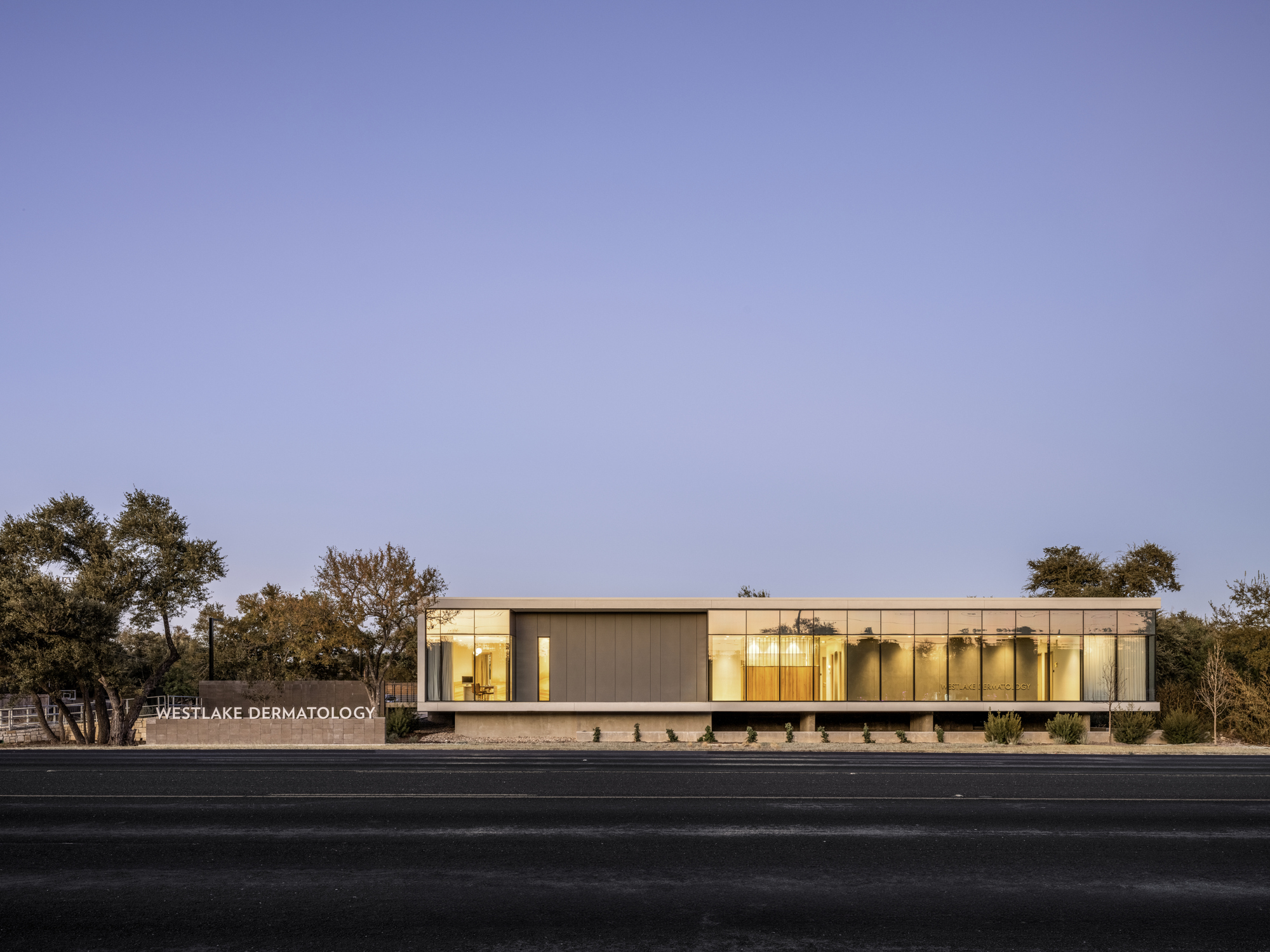 Front elevation showing the low horizontal volume with illuminated interior at dusk