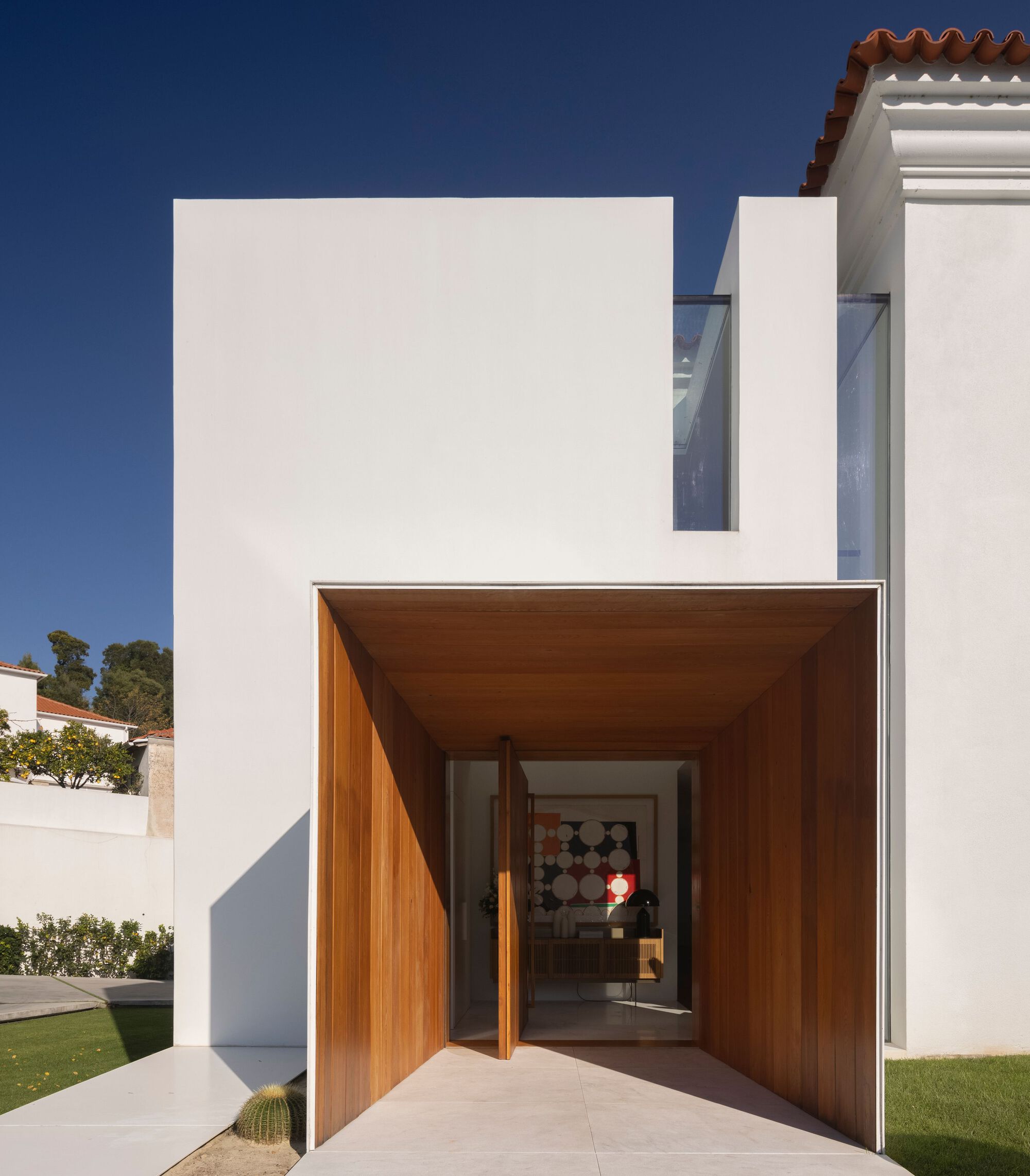 Recessed entry portal clad in timber with pivoting door opening to the interior under clear blue sky