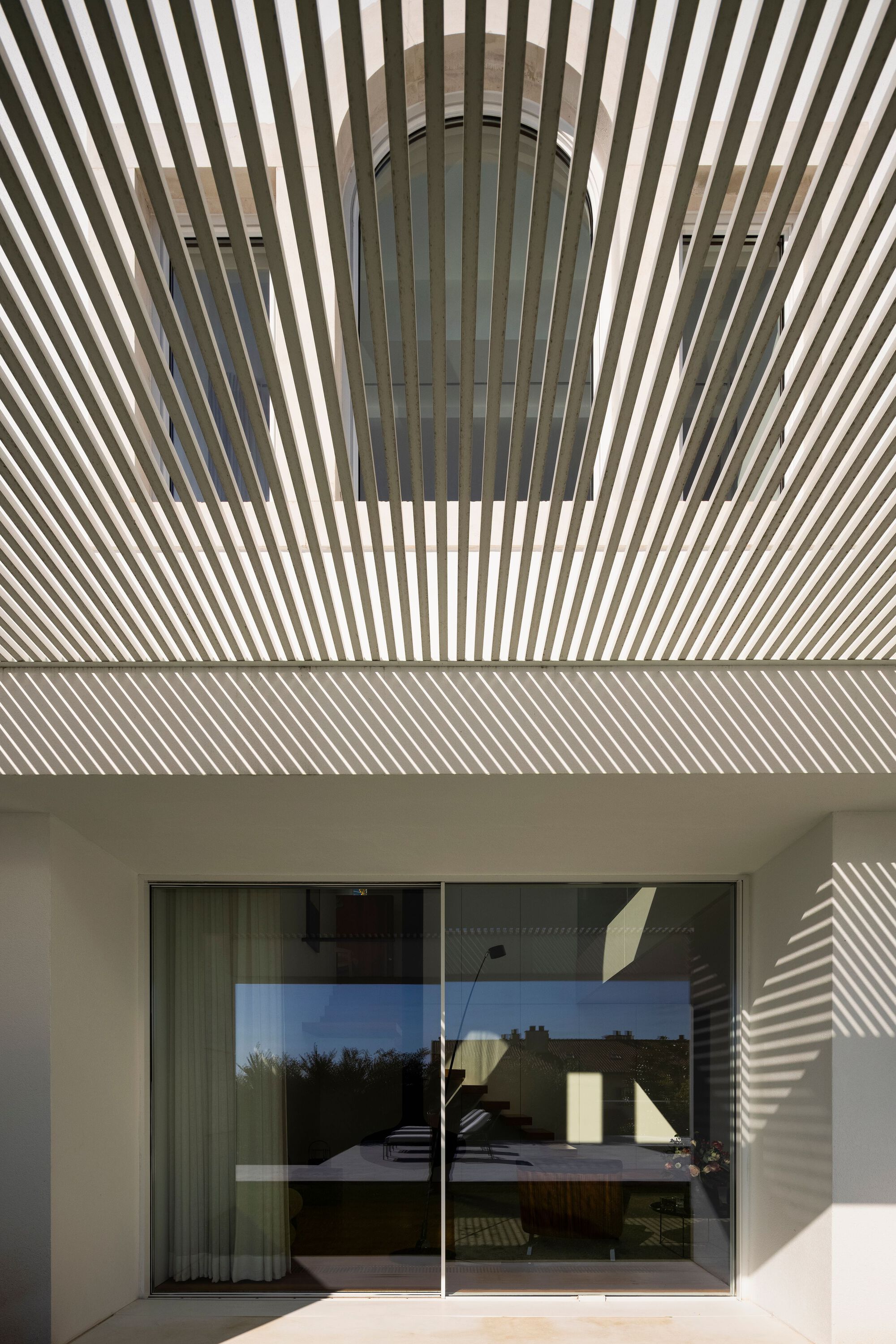 Timber slat pergola casting striped shadows on the wall and glass door below