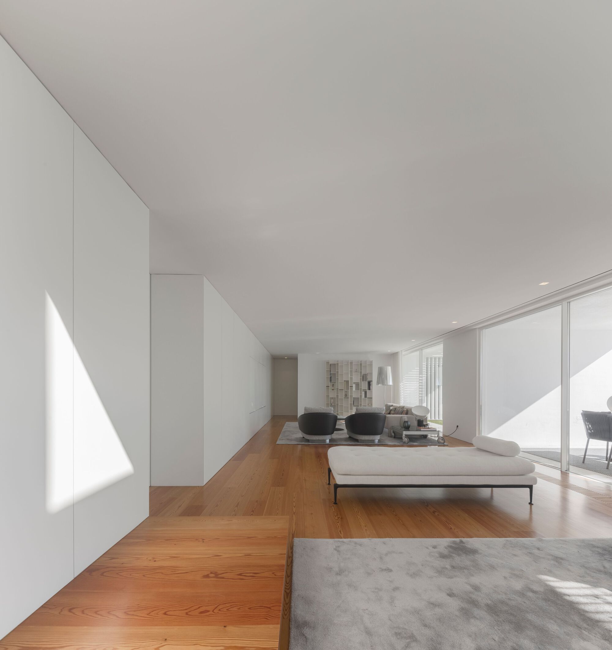 Open living space with white walls and timber flooring illuminated by diagonal bands of sunlight