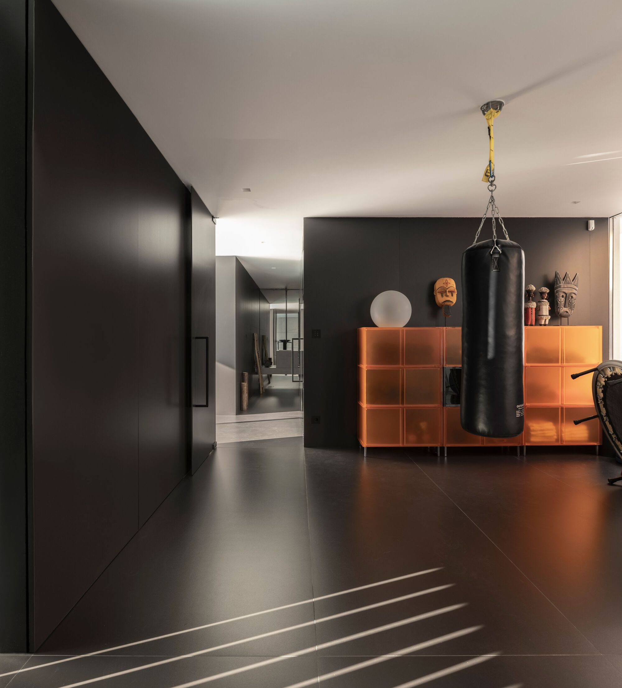Dark corridor with orange storage units and a suspended punching bag beneath recessed ceiling lighting