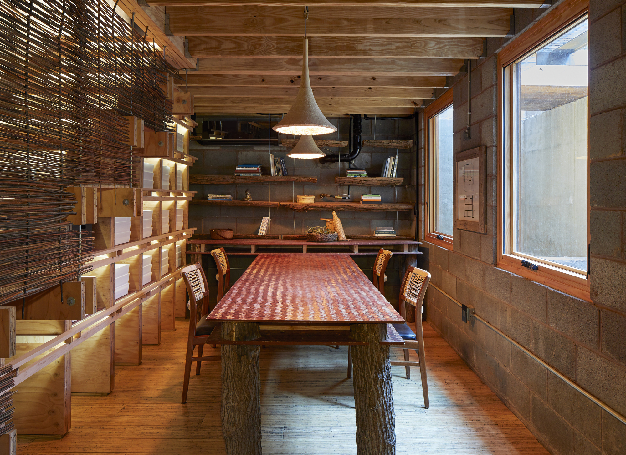 Dining room with exposed timber ceiling beams, horizontal wood shelving and woven screen partition wall