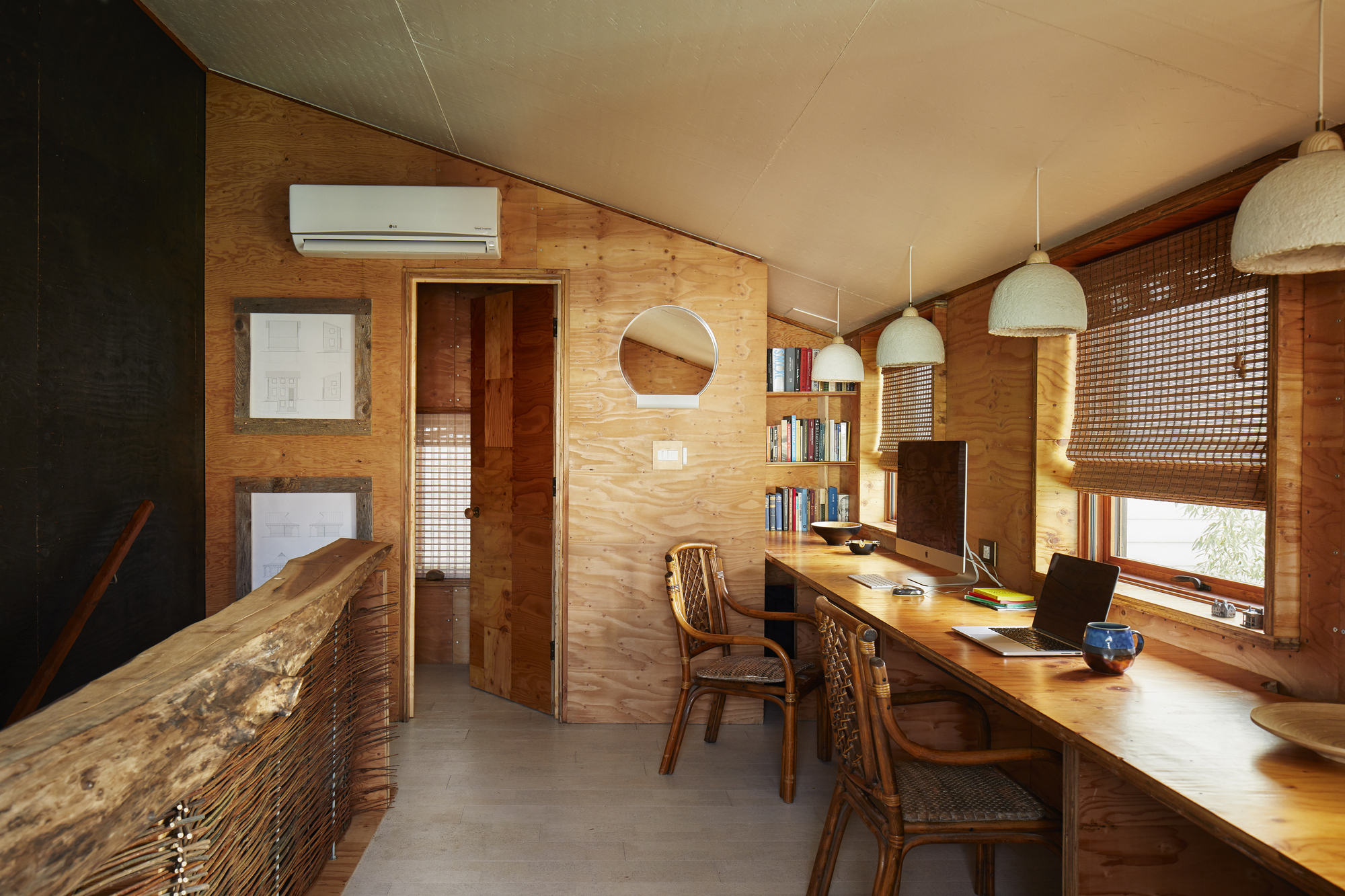 Study area with plywood walls, built-in desk and woven lattice window shades in afternoon light