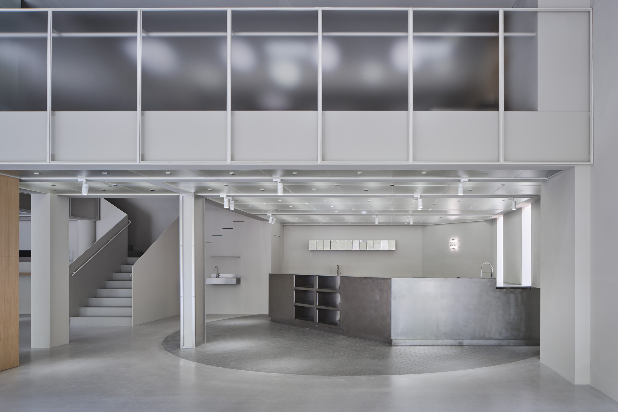 Ground floor sales area with curved counter, floating staircase, and suspended mezzanine framed by white columns