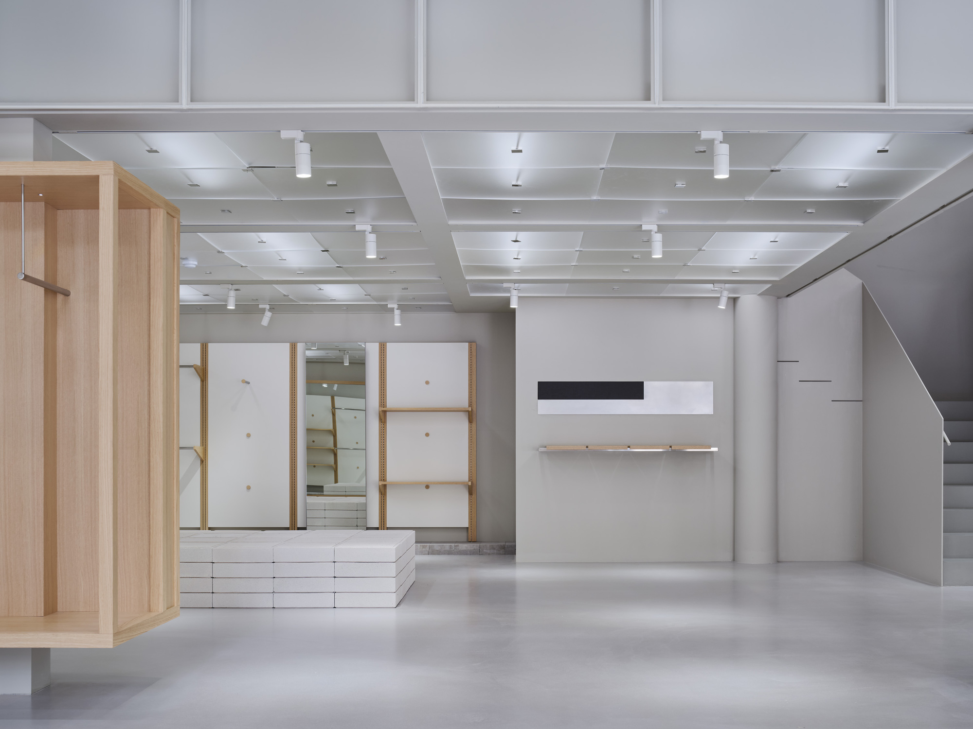 Interior view showing light wood framed display niches, white shelving, and cofferred ceiling with pendant lighting