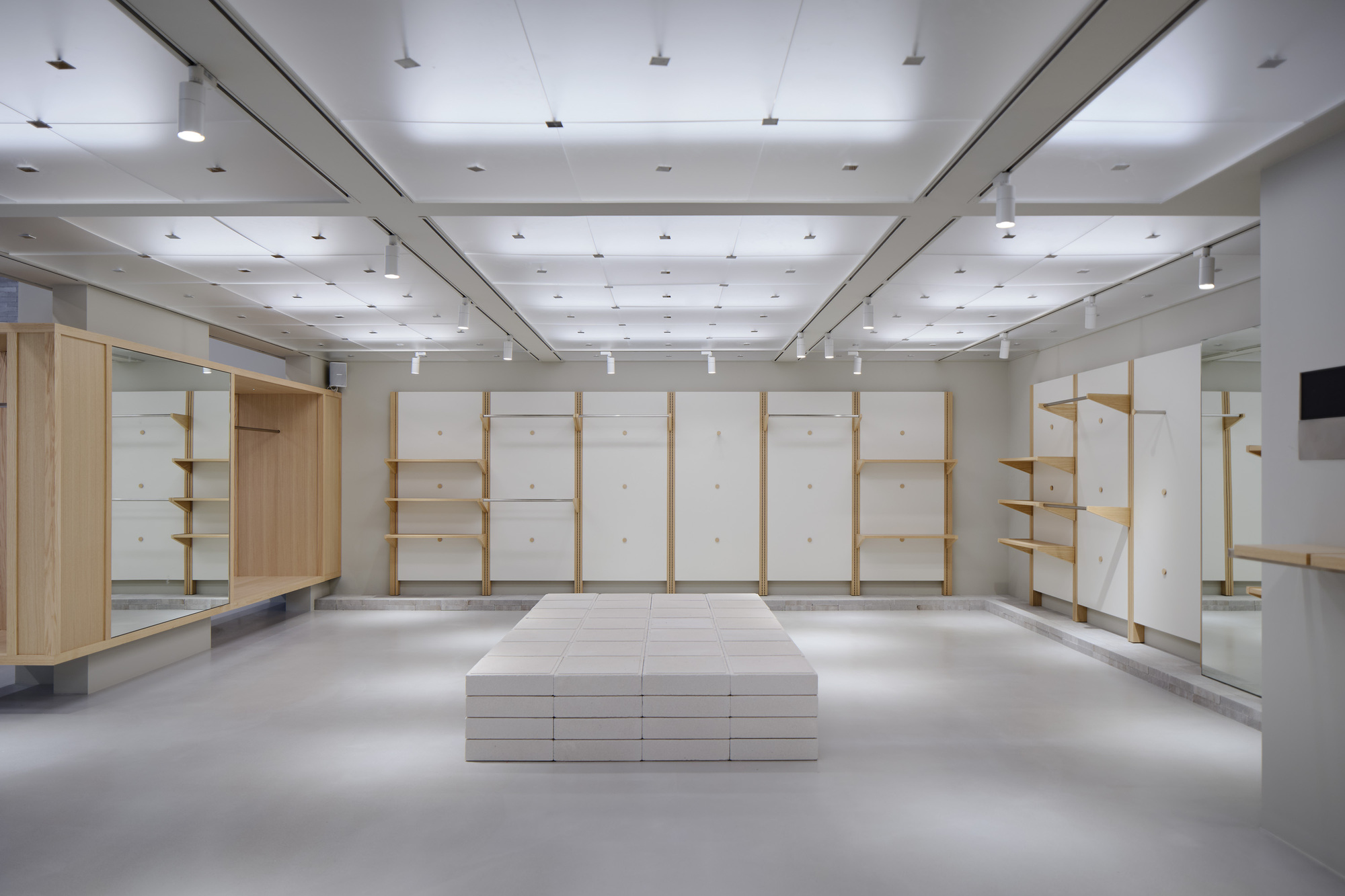 Retail interior with timber and white panel shelving units around a central platform under track lighting