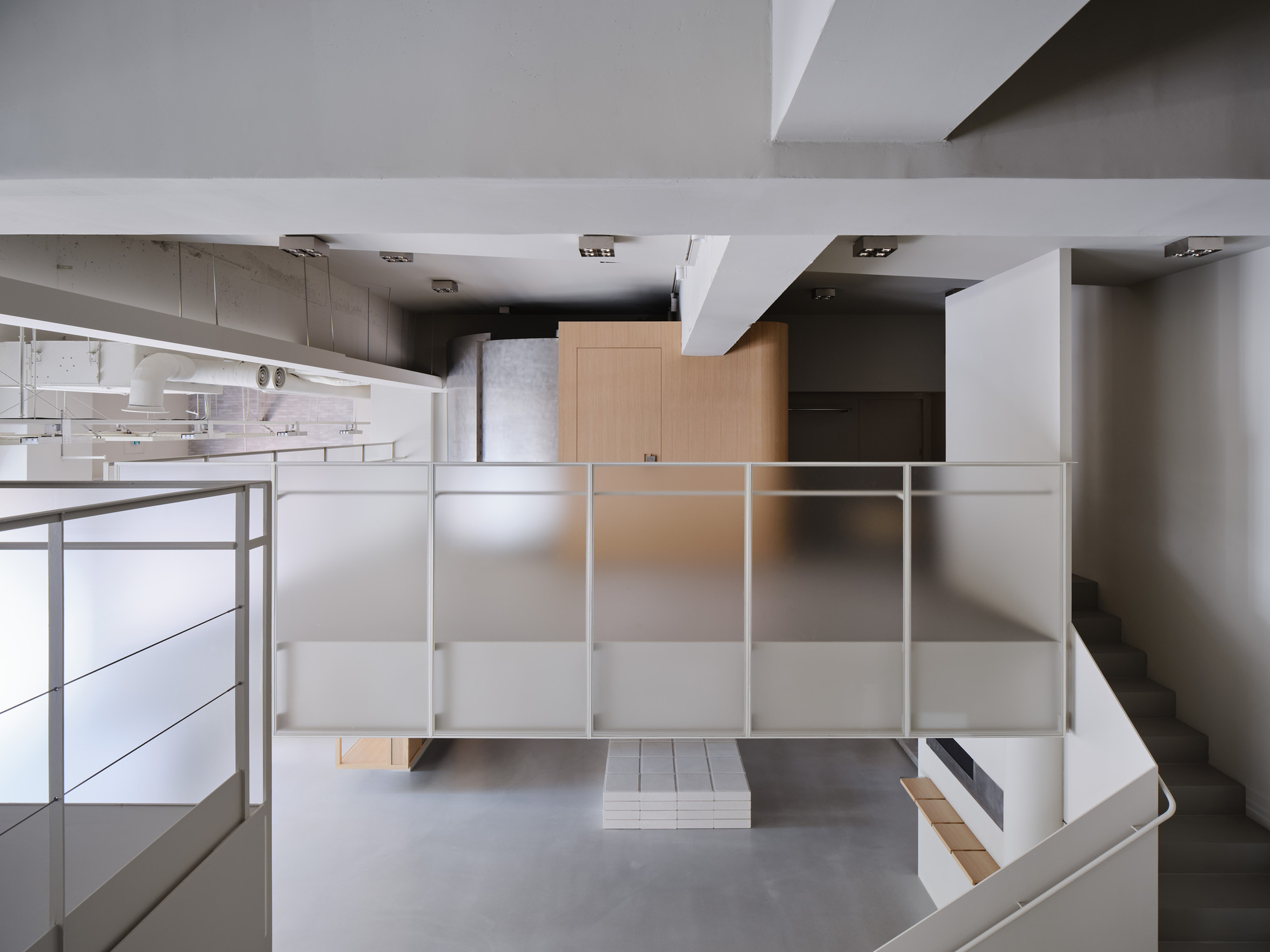 Top-down view of a double-height interior with translucent partitions and metal railings below skylights