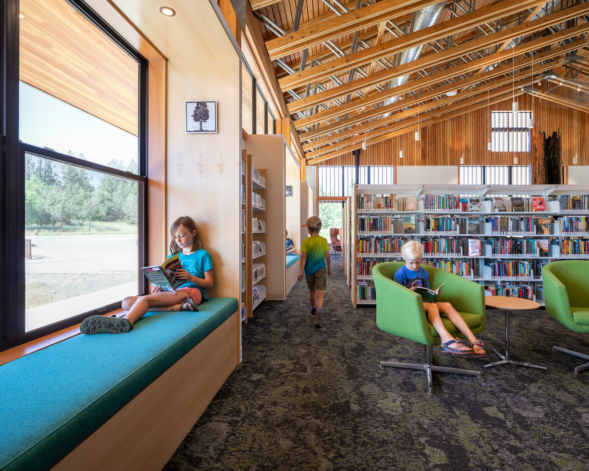 Library interior showing built-in window seat along glazed wall with children reading throughout the carpeted space
