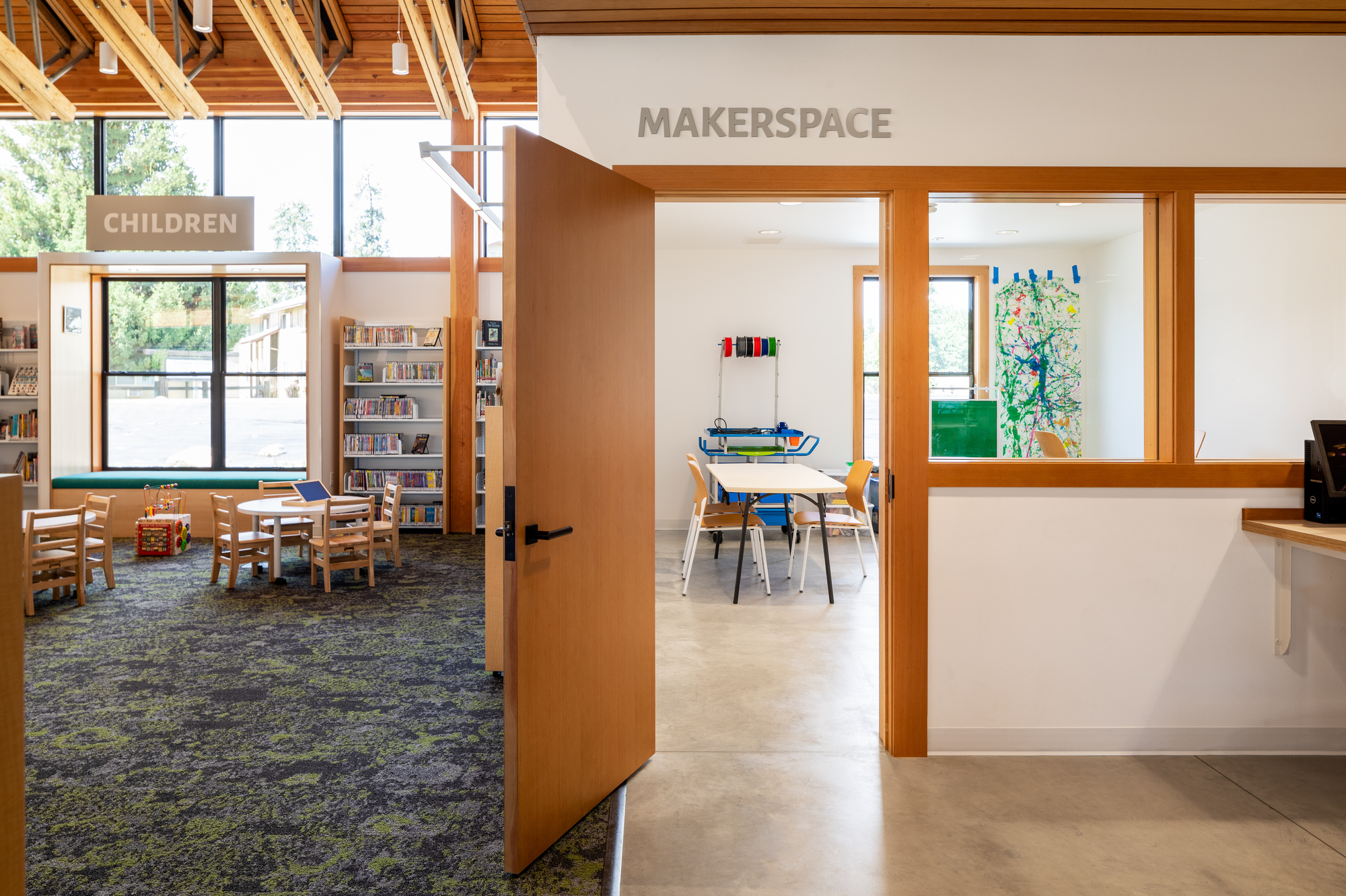 Open doorway between children's area and makerspace with exposed timber roof framing overhead