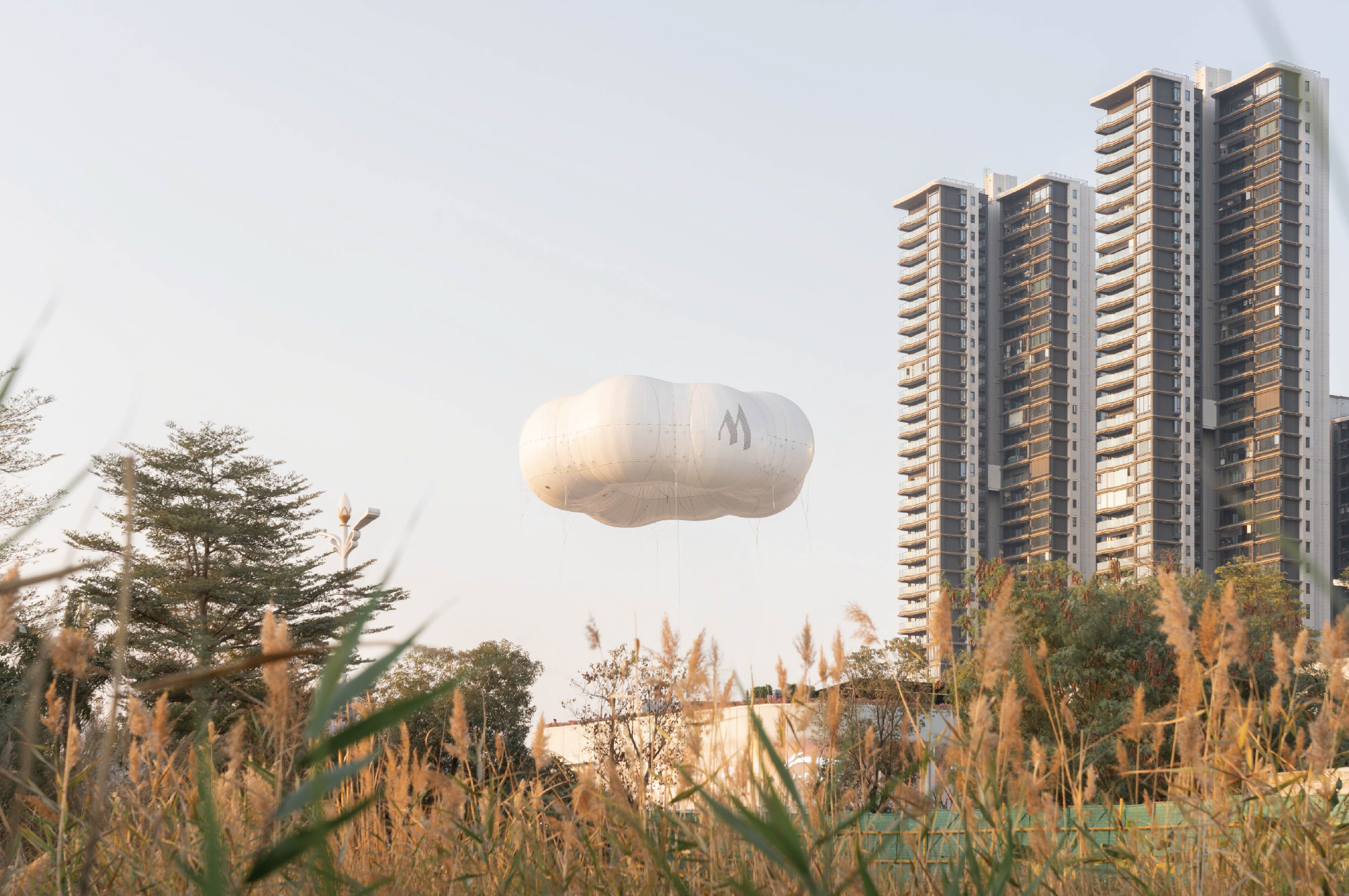 Airborne white fabric balloon floating above ornamental grasses with residential towers in the distance