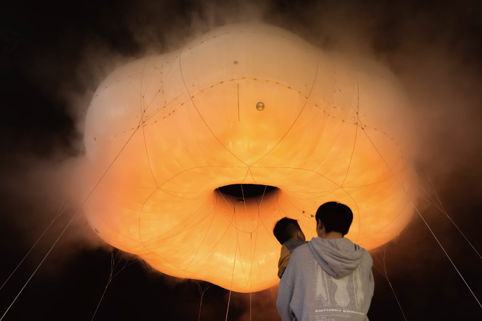 Interior view of orange lit fabric membrane with two visitors looking up at seamed canopy structure