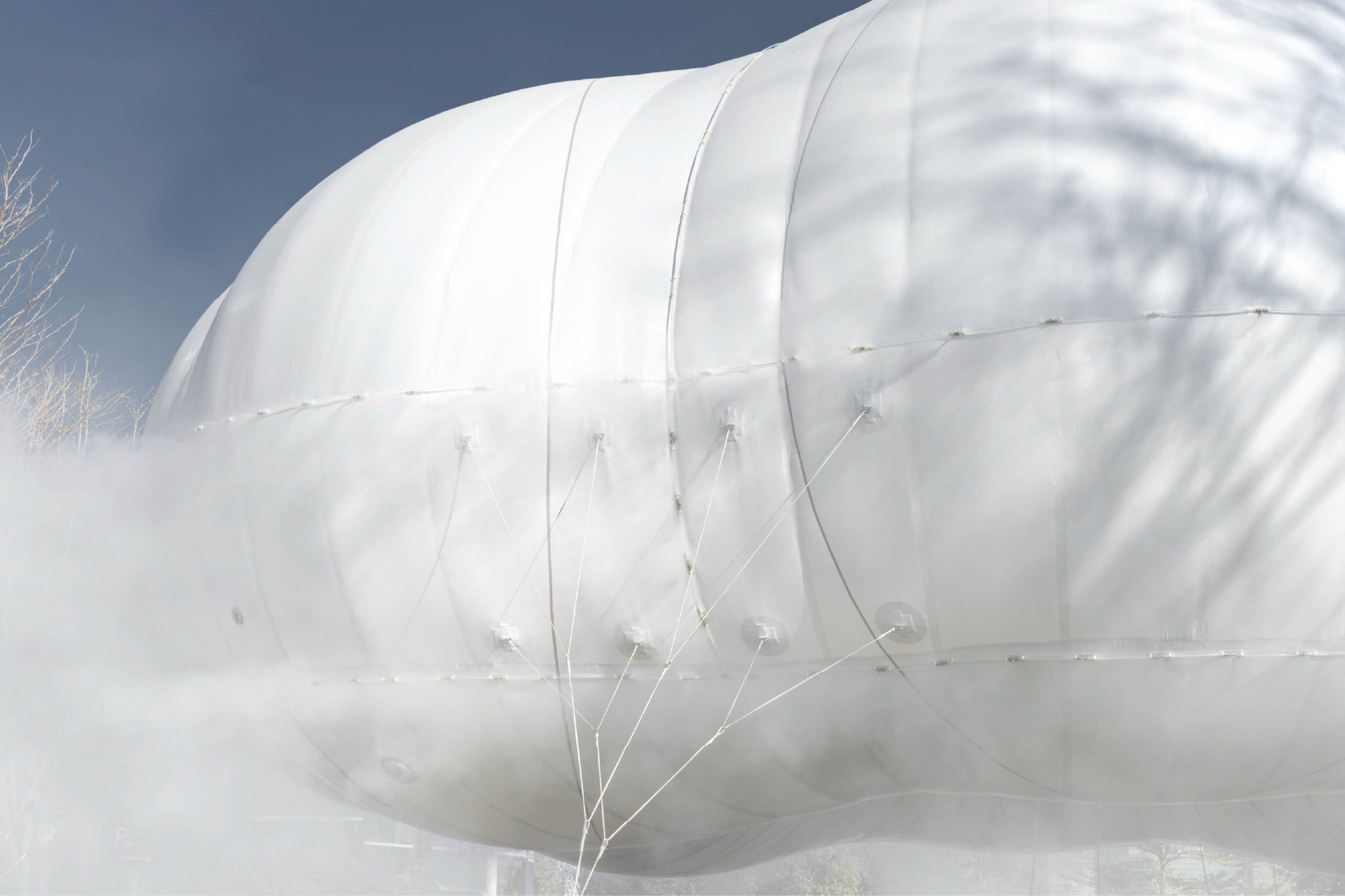 Close-up of the tensioned white membrane surface with tether lines and seams under a cloudy sky