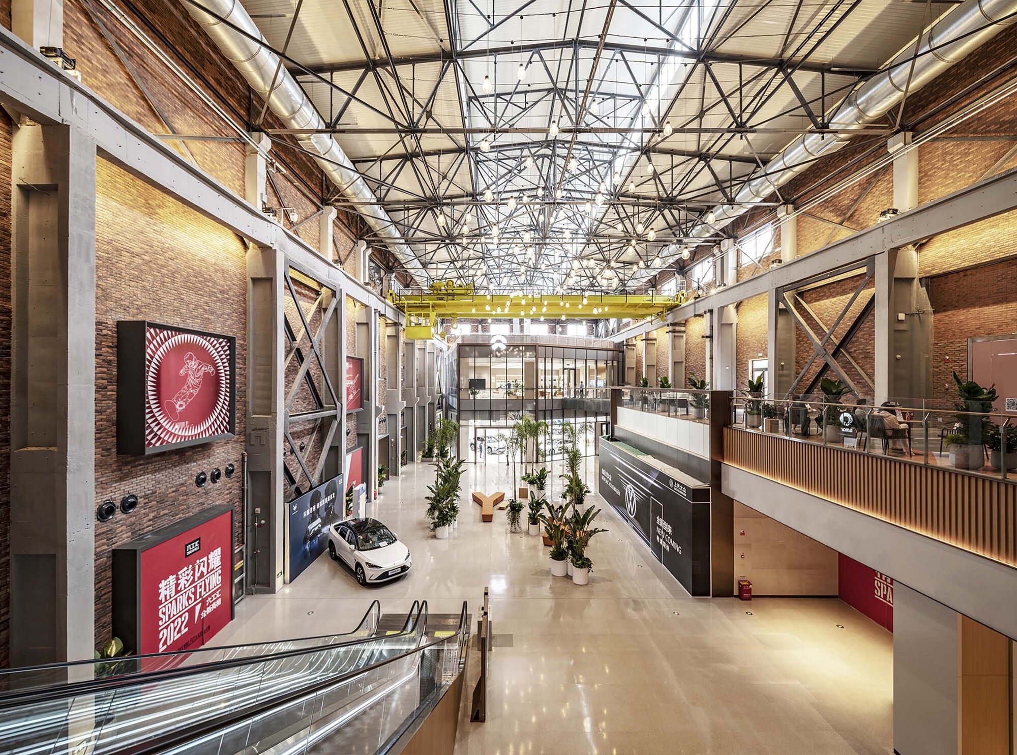 Interior hall with exposed steel trusses, brick walls, mezzanine levels and a display car on polished floor