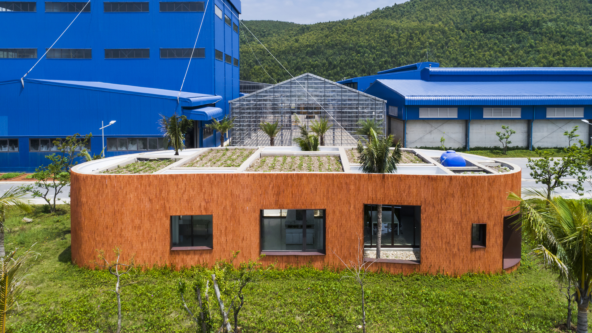 Planted green roof atop the curved brick structure with blue industrial buildings behind