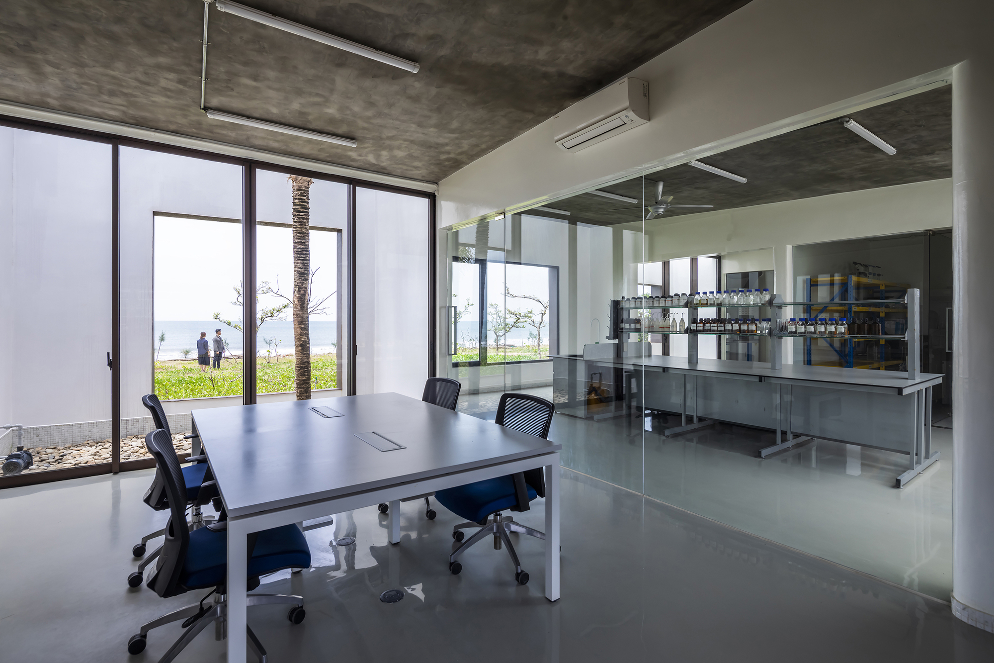 Interior workspace with glass partition separating meeting area from stainless steel equipment beyond full-height glazing
