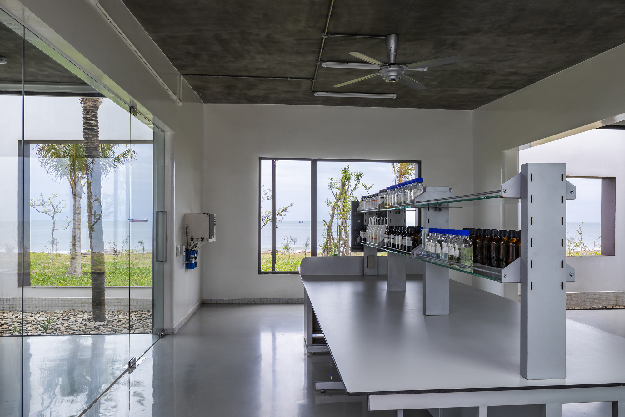 Stainless steel bottling equipment beneath exposed concrete ceiling with ceiling fan and courtyard views