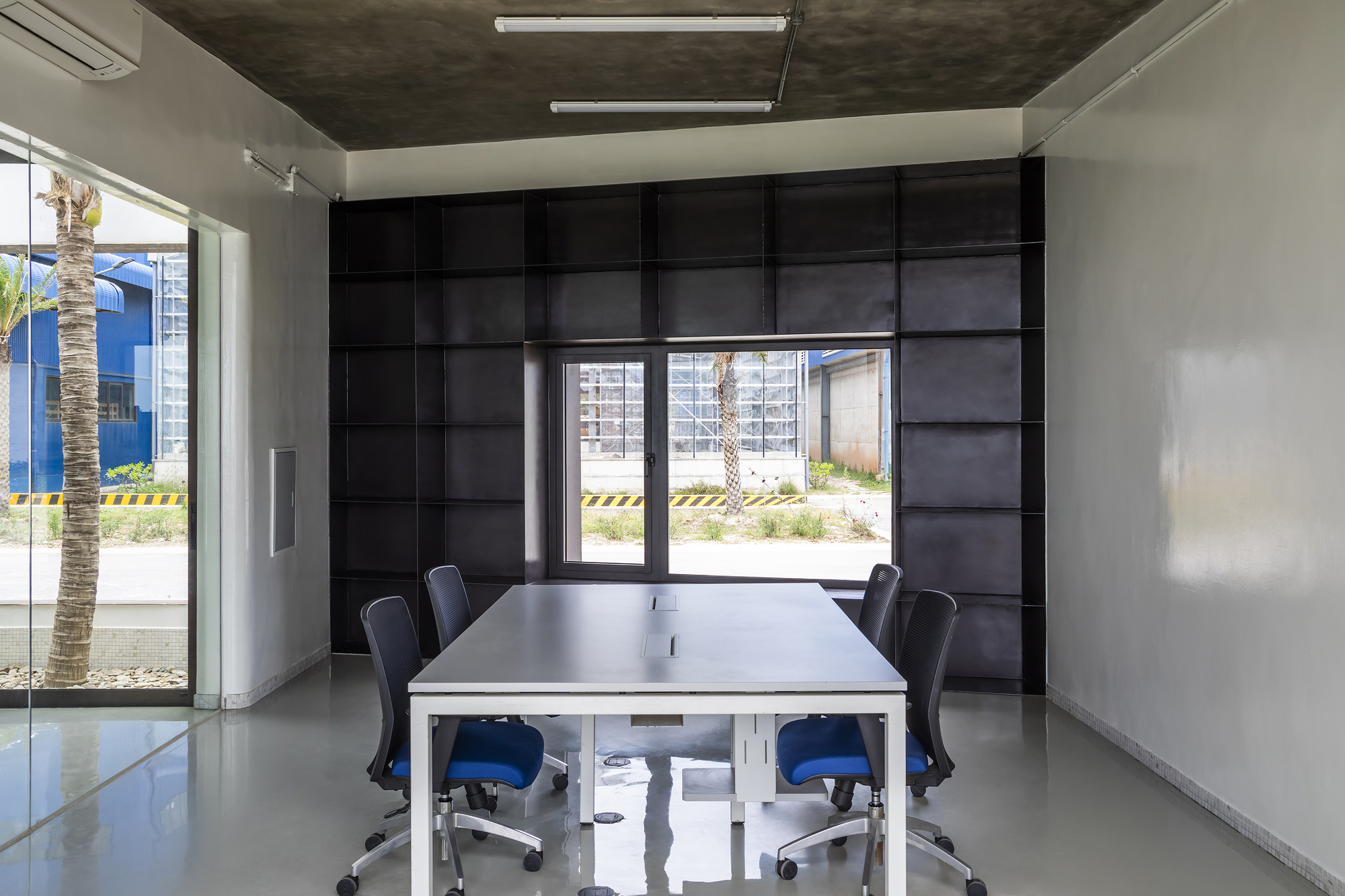 Conference room with black paneled wall and central framed window overlooking a palm tree courtyard