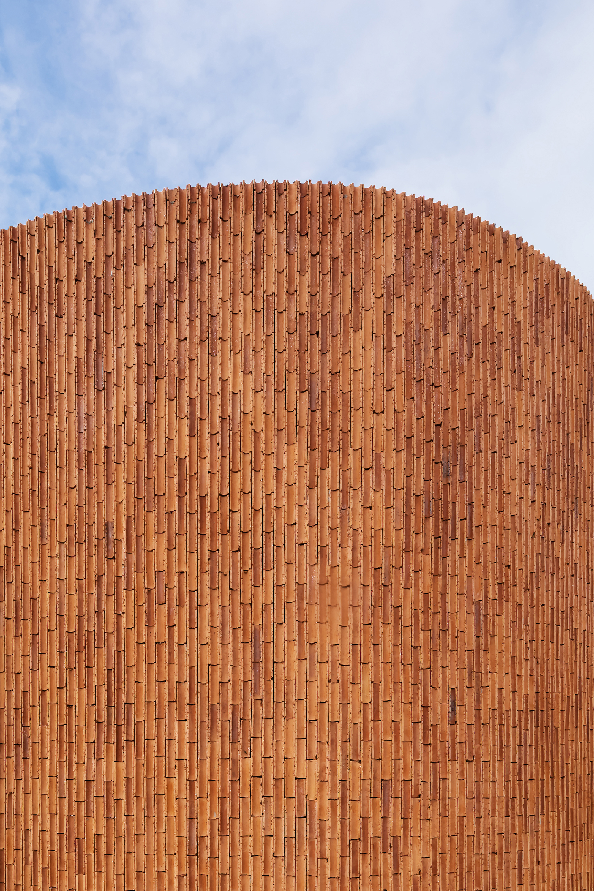 Curved terracotta brick facade rising against a partly cloudy sky