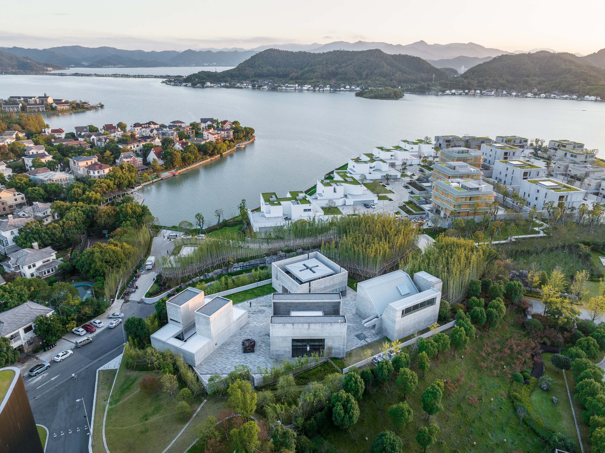 Drone view of the clustered white volumes among green landscape overlooking a lake and distant mountains at dusk