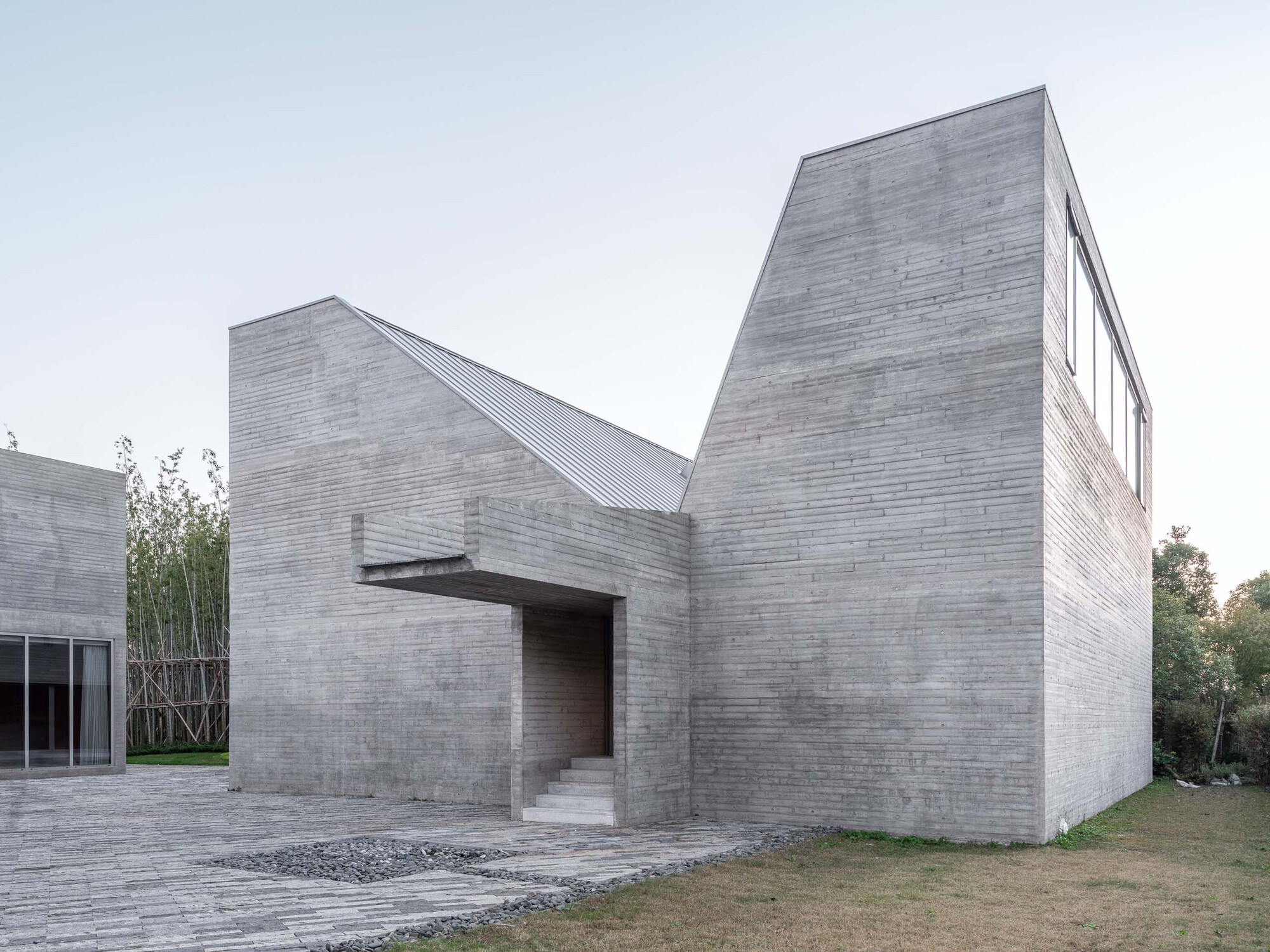 Entrance facade with cantilevered canopy and angled brick volumes flanked by bamboo and gravel paths